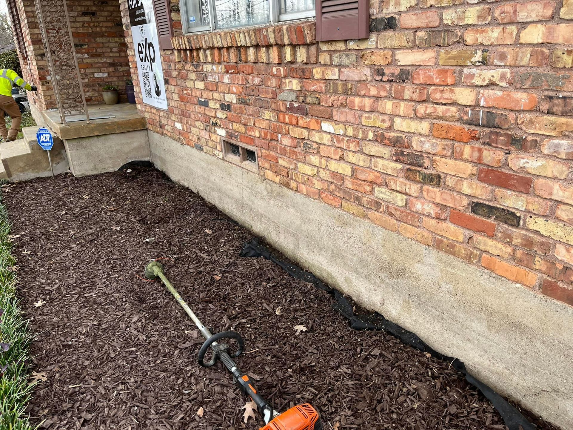 A lawn mower is sitting on the ground in front of a brick house.
