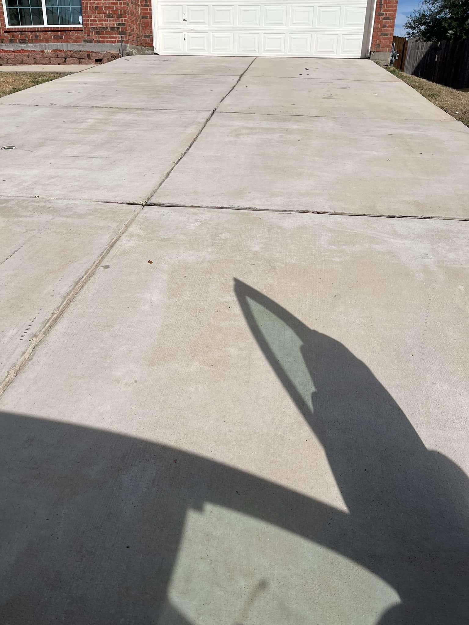 A shadow of a car is cast on a concrete driveway in front of a garage door.