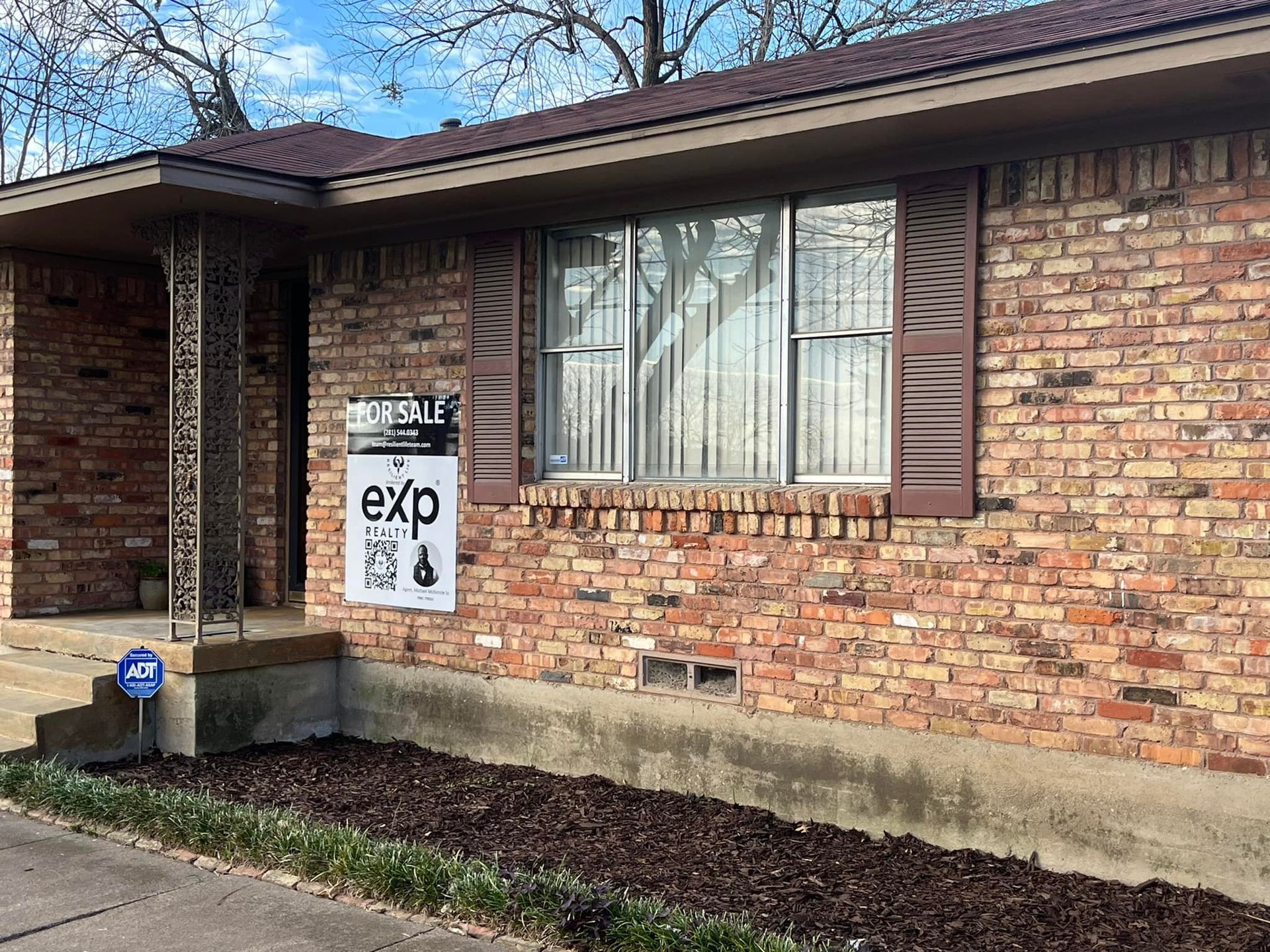 A brick house with a for sale sign in front of it.