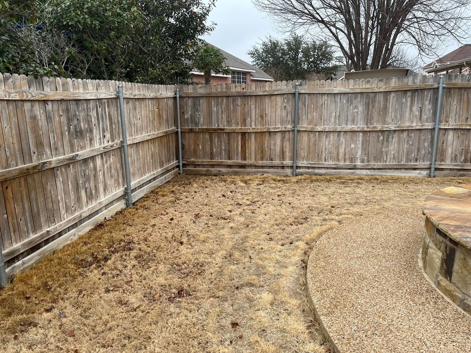 A wooden fence surrounds a gravel area in a backyard.