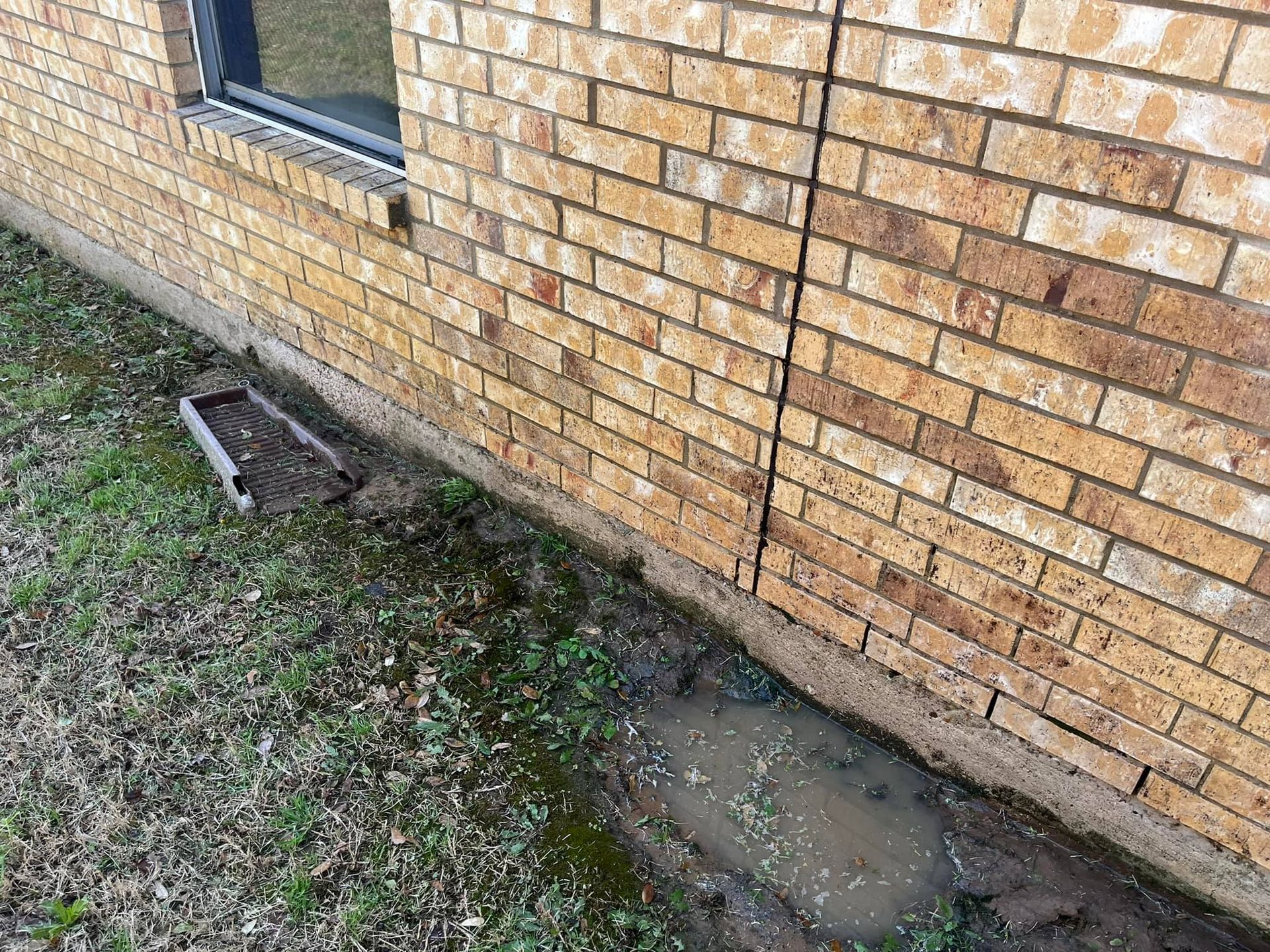 A brick wall with a window and a puddle of water on the side of it.
