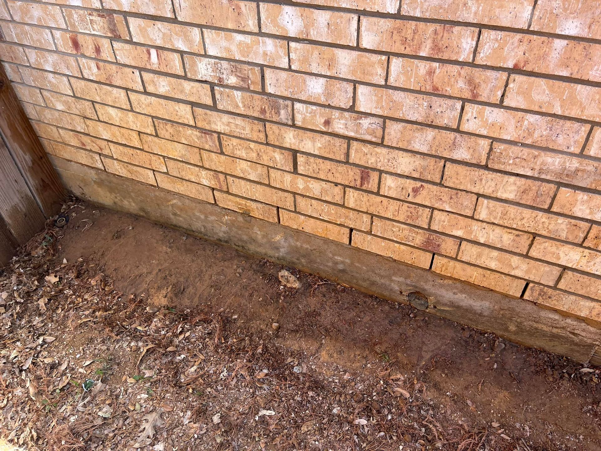 A brick wall with a lot of dirt on the ground in front of it.