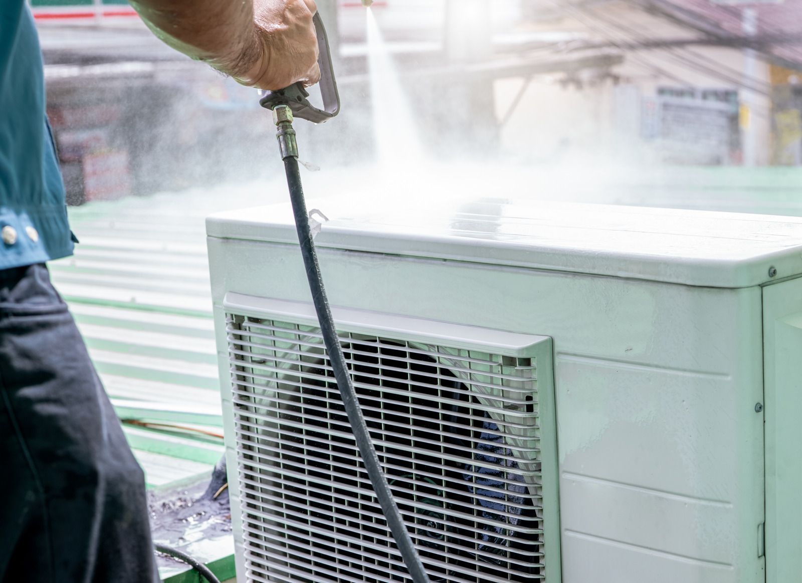 Person power washing an outdoor air conditioning unit.