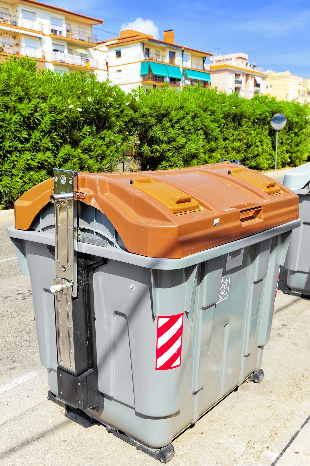 A large trash can with a brown lid is parked on the side of the road.