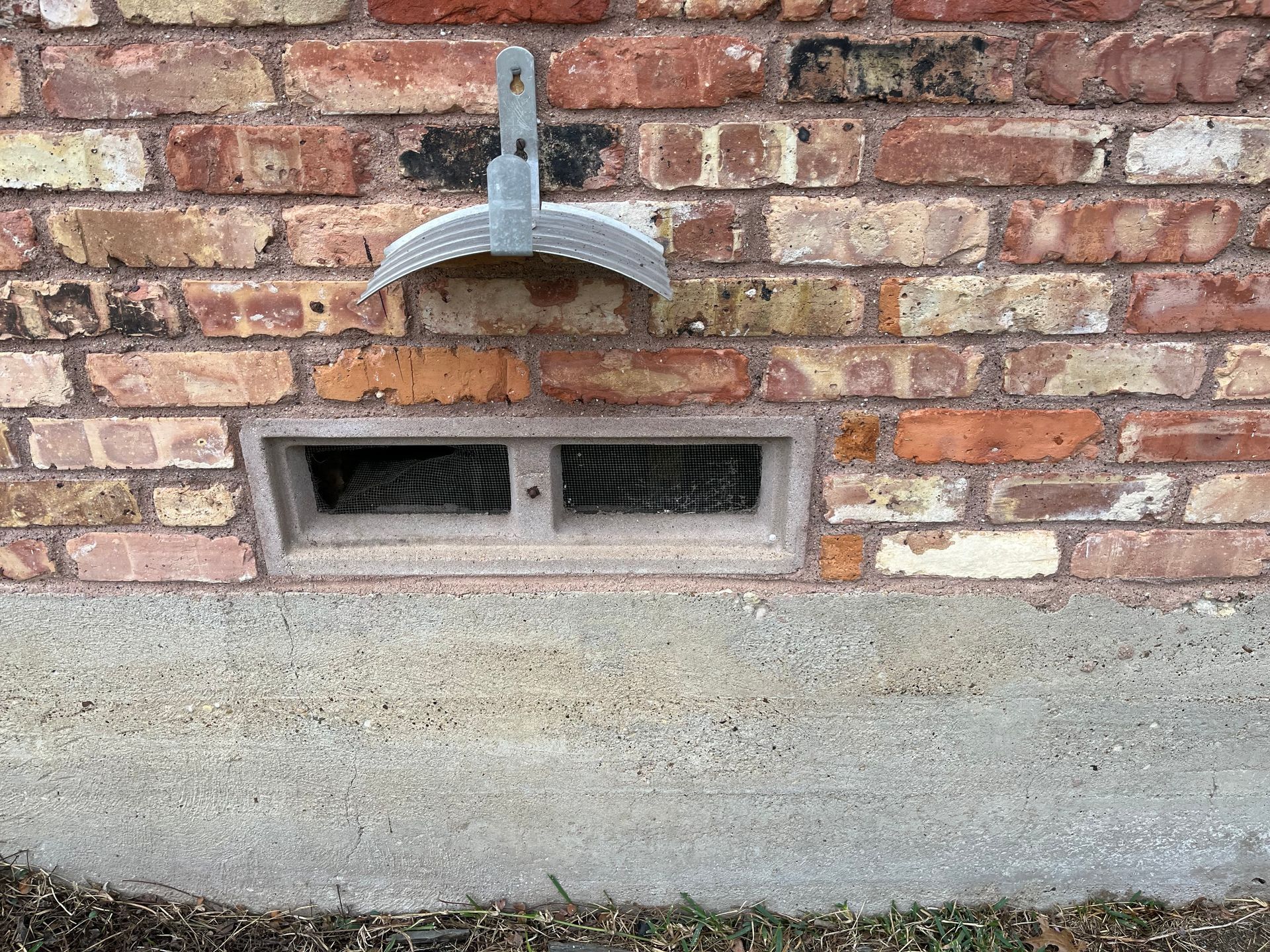 A brick wall with a window and a shovel hanging from it.