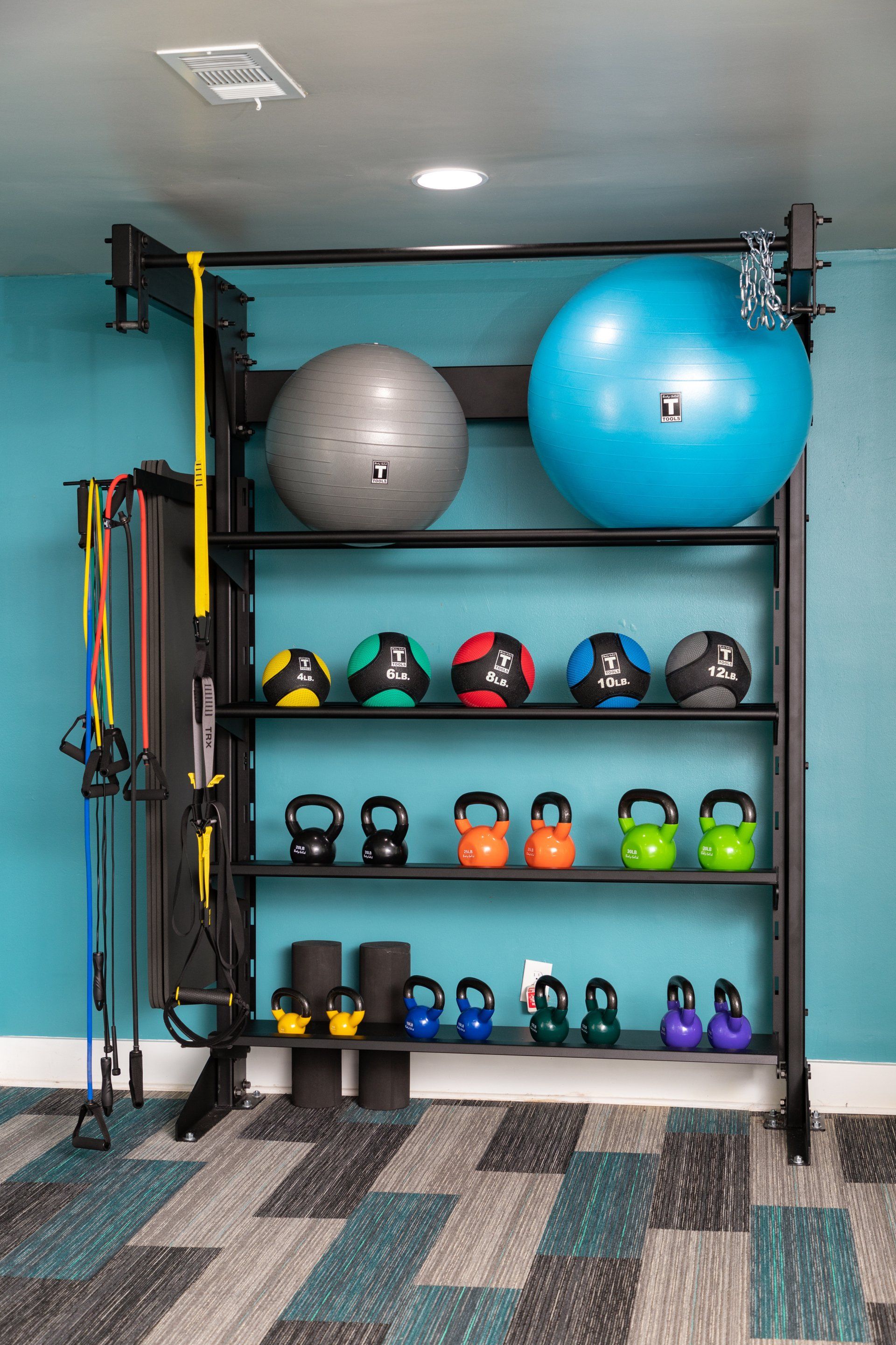 A gym with a shelf filled with exercise balls and kettlebells.