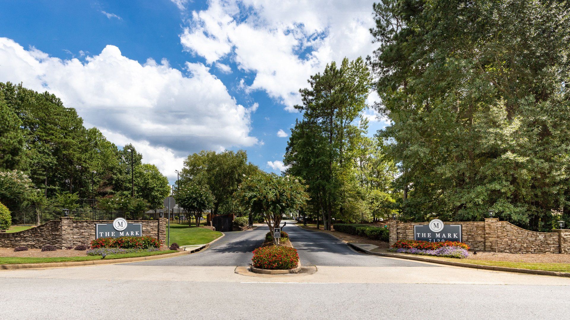 The entrance to a gated community with trees and a stone wall.