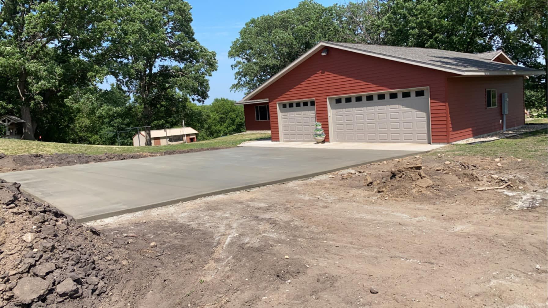 A red house with two garage doors and a concrete driveway in front of it.