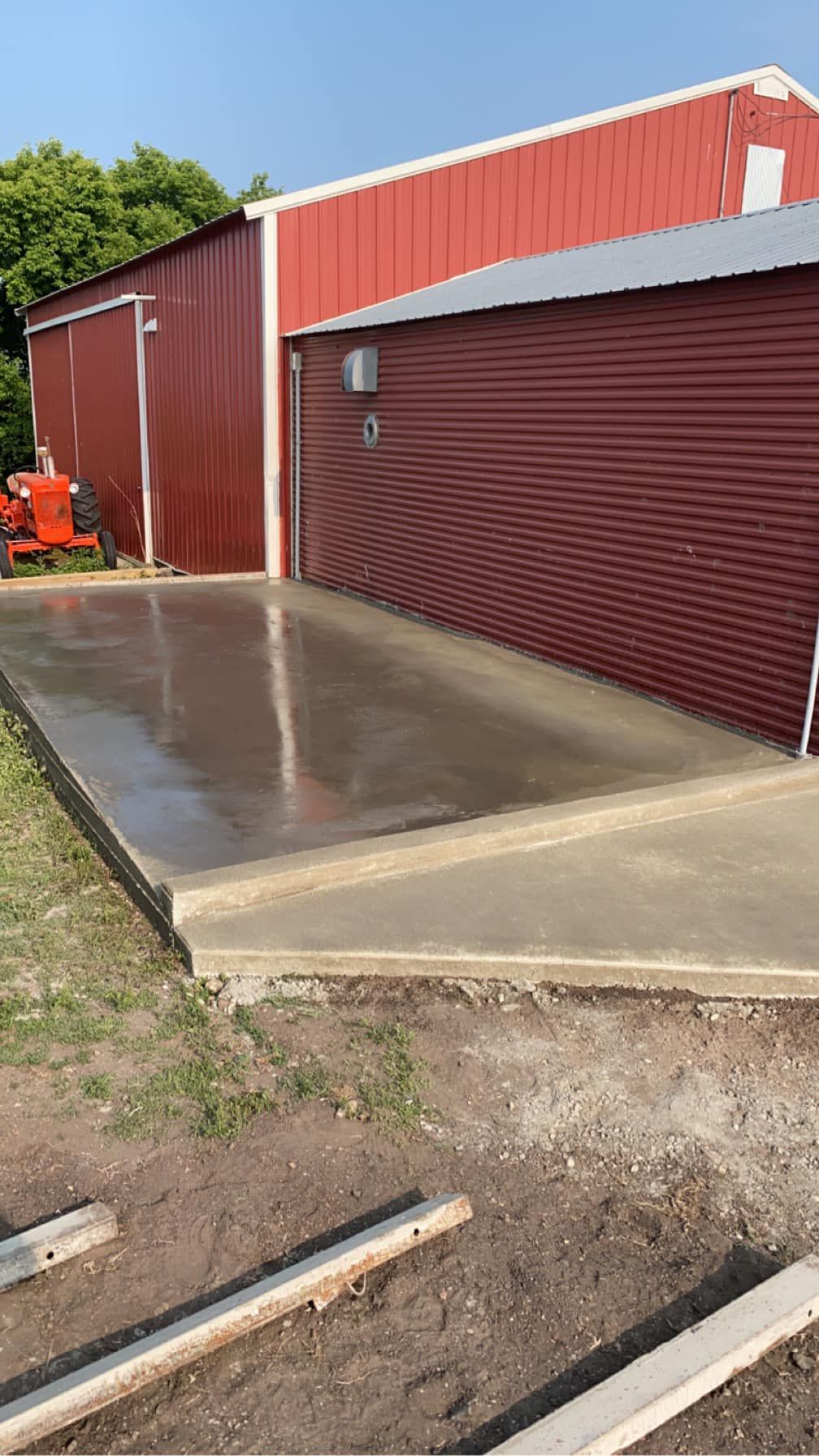A concrete driveway is being built in front of a red barn.