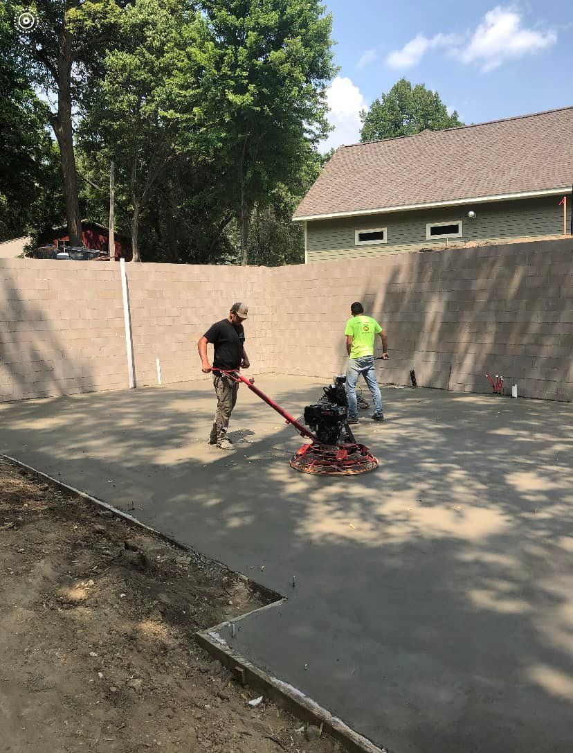 Two men are working on a concrete driveway in front of a house.