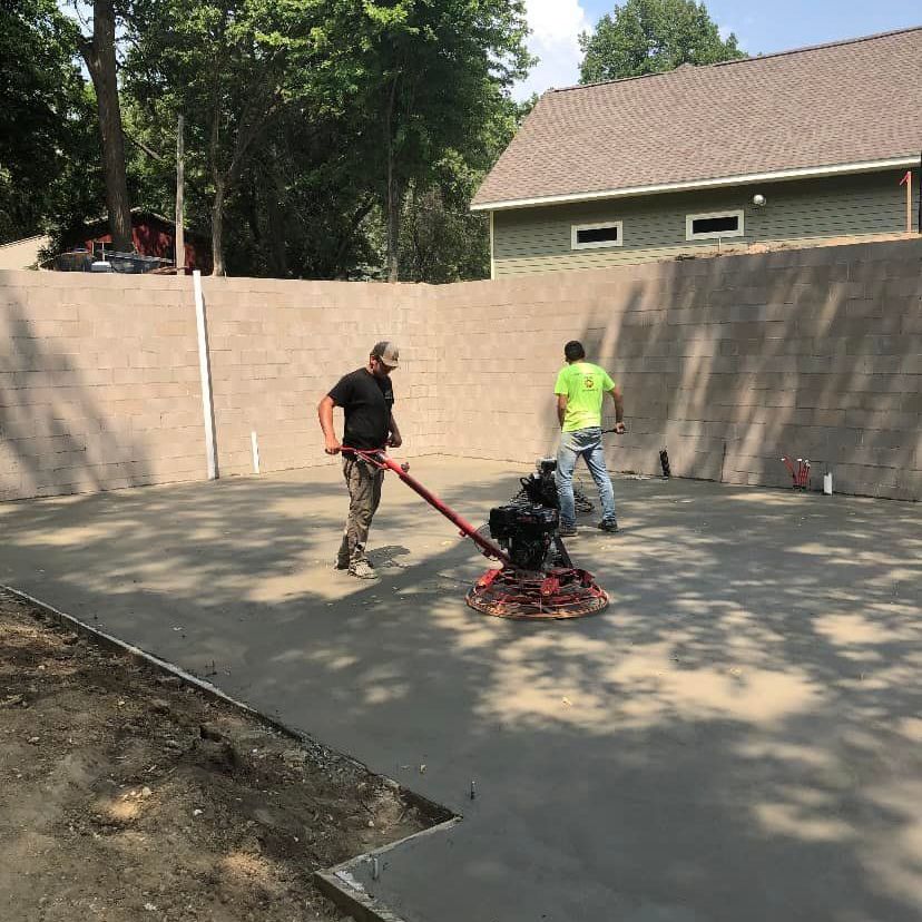 Two men are working on a concrete driveway in front of a house
