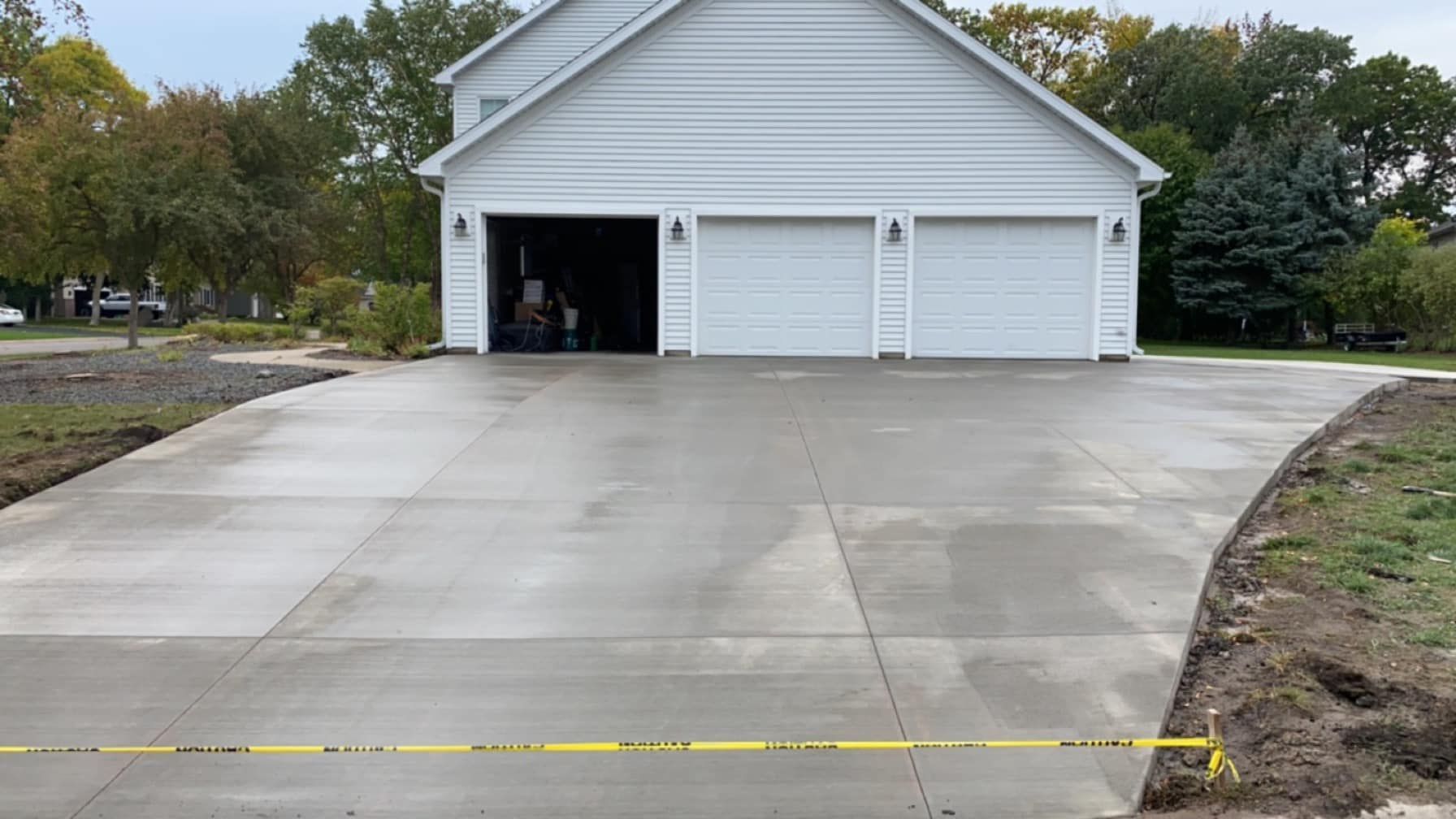 A white garage with three garage doors and a concrete driveway leading to it.