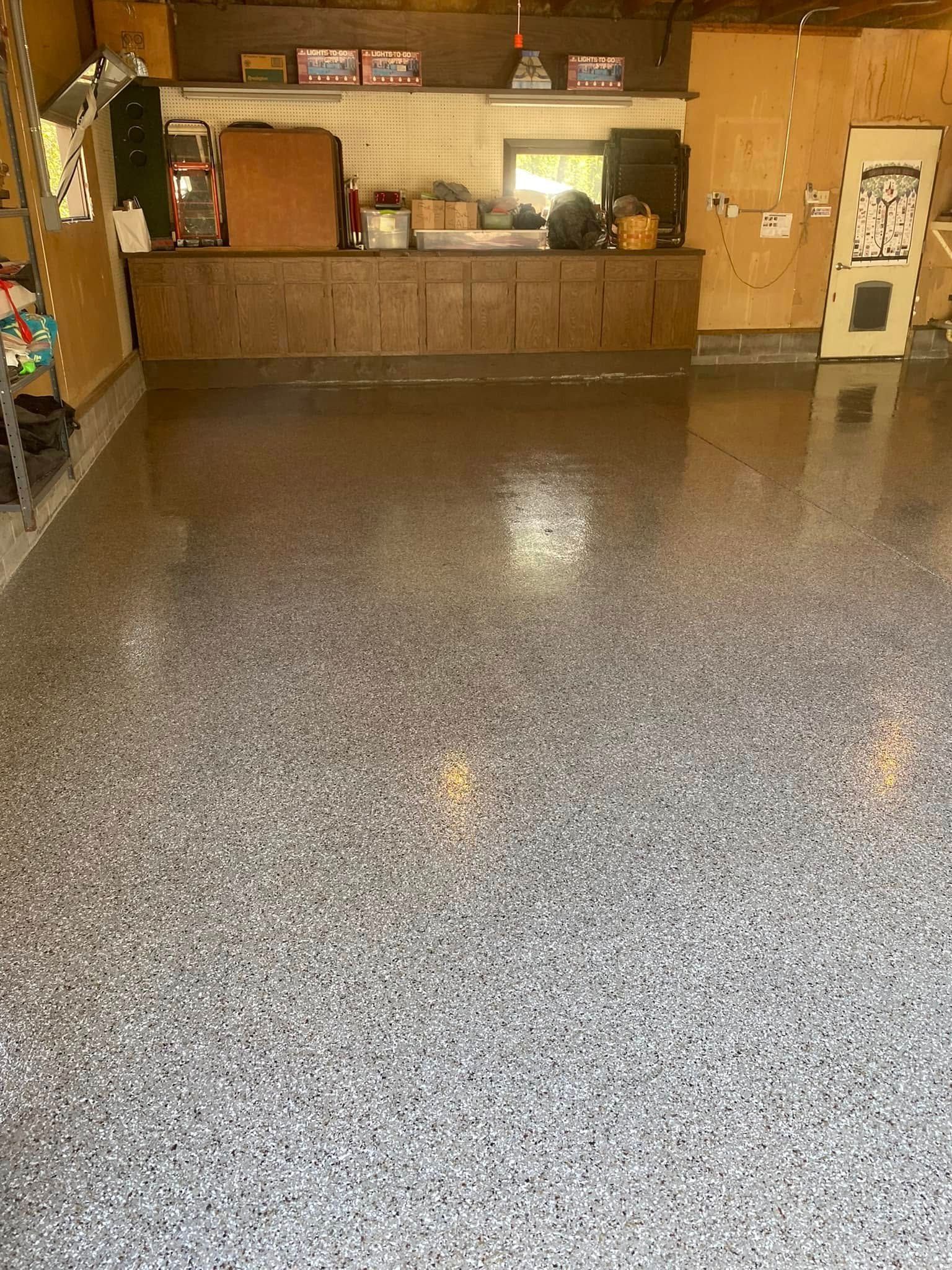 A garage with a gray epoxy floor and wooden cabinets.