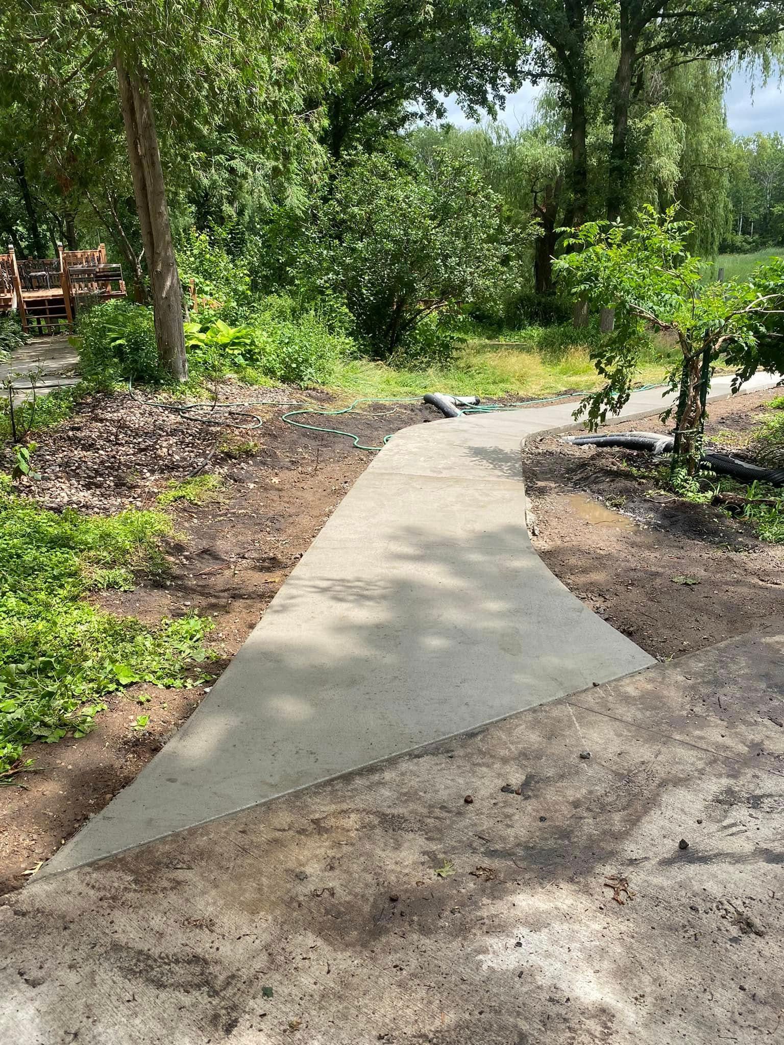 A concrete walkway in the middle of a park surrounded by trees.