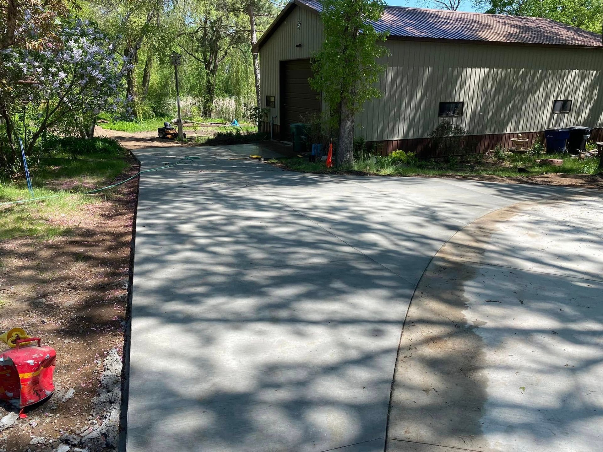 A concrete driveway leading to a garage with a barn in the background.