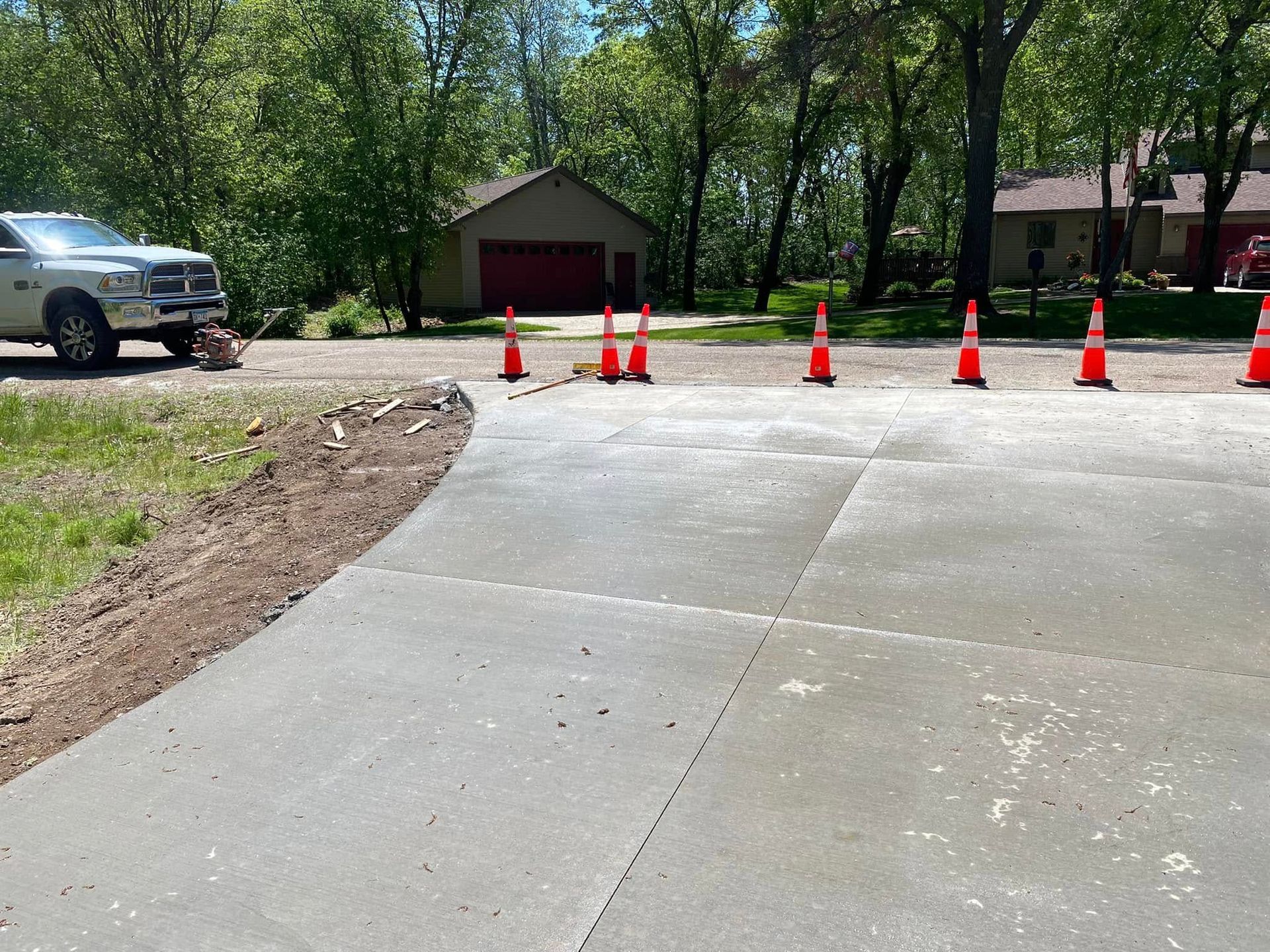 A white truck is parked on a concrete driveway next to a row of orange traffic cones.