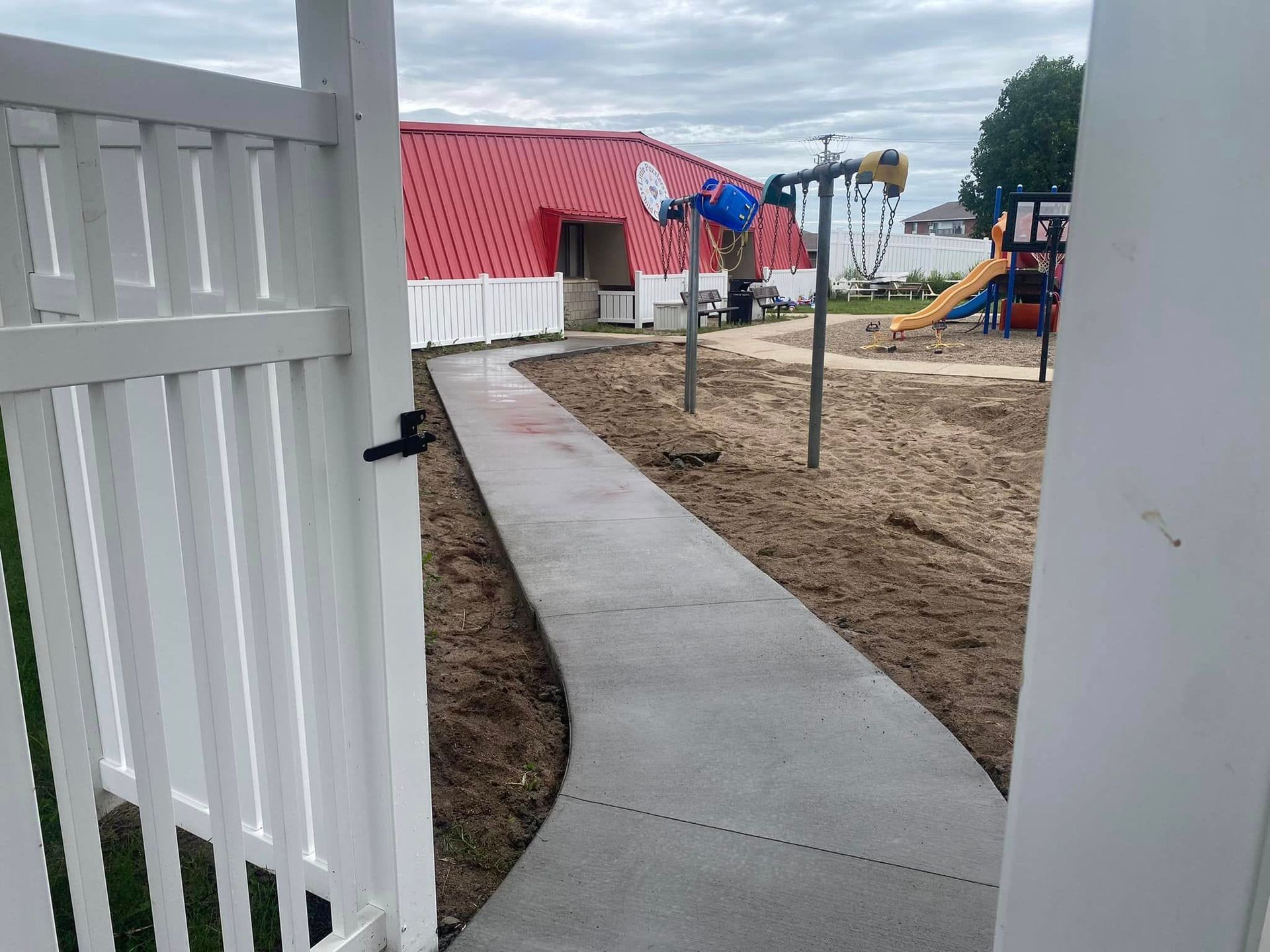 A white fence leading to a playground with a red building in the background.