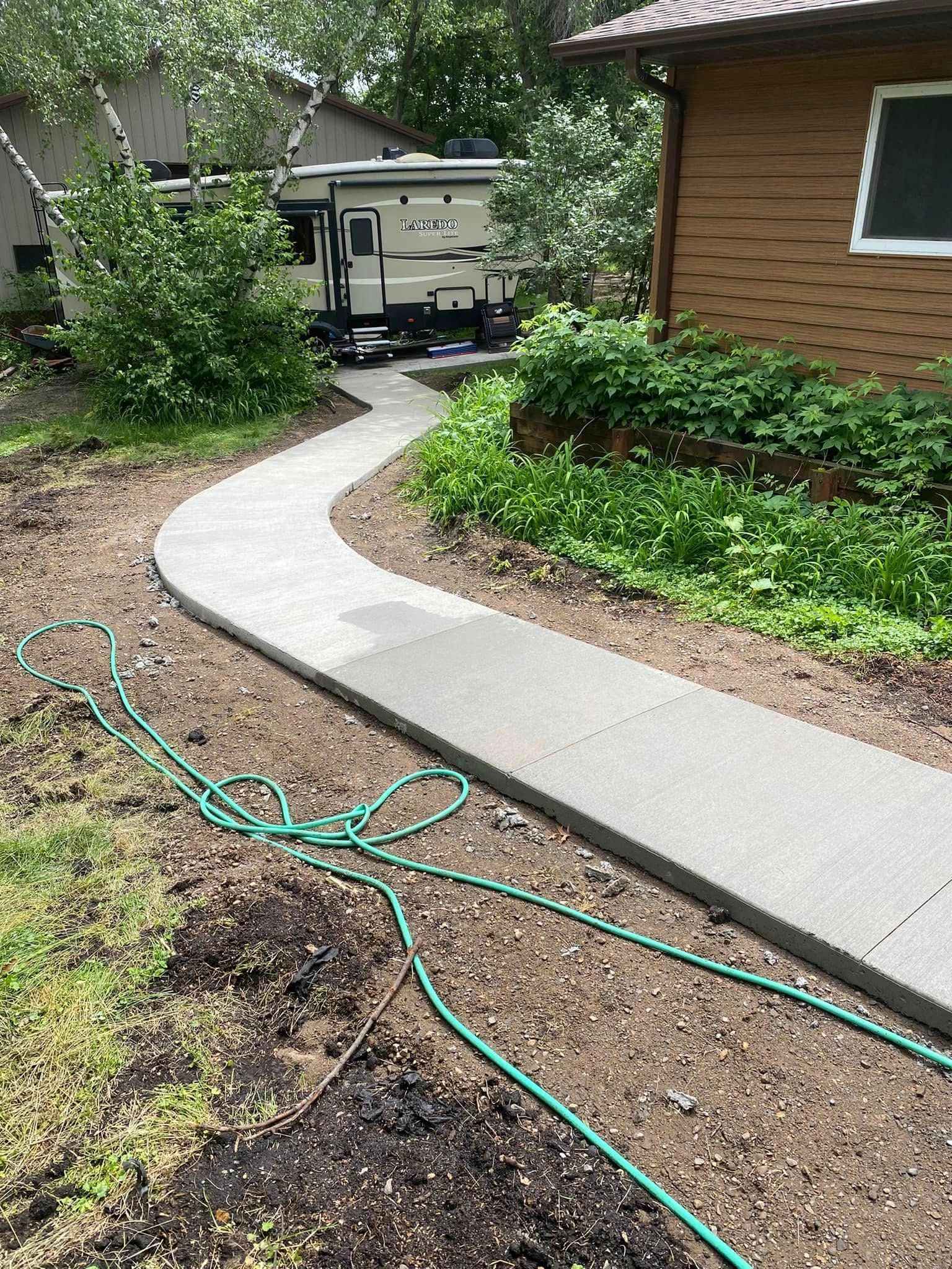 A concrete walkway leading to a house with a hose attached to it.