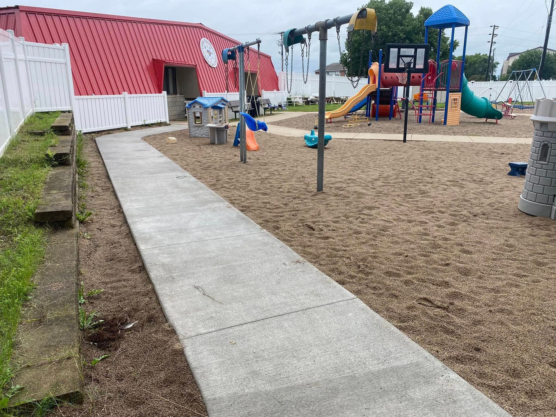 A concrete walkway leading to a playground with a red building in the background.