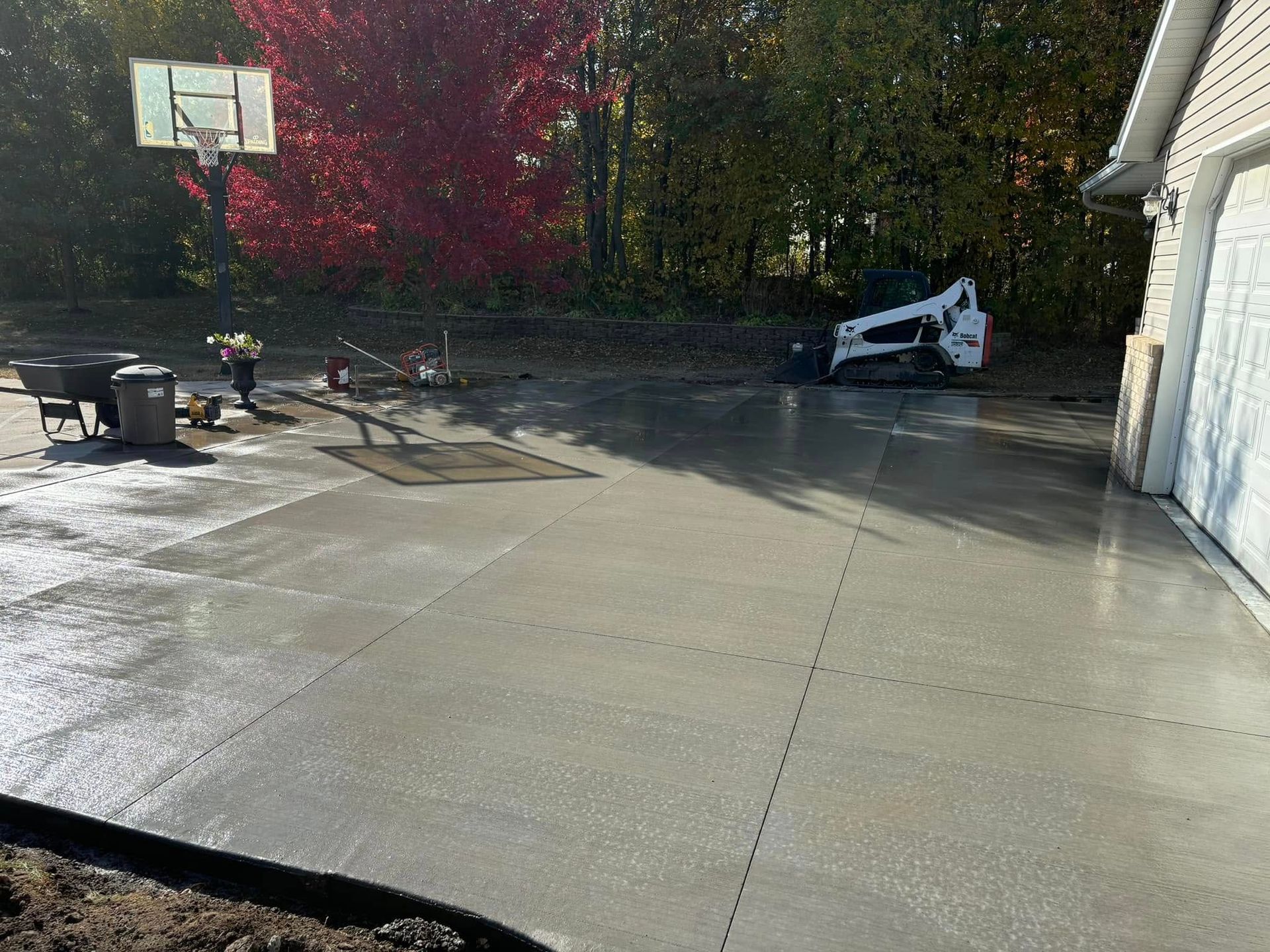 A basketball hoop is being built in a driveway next to a house.