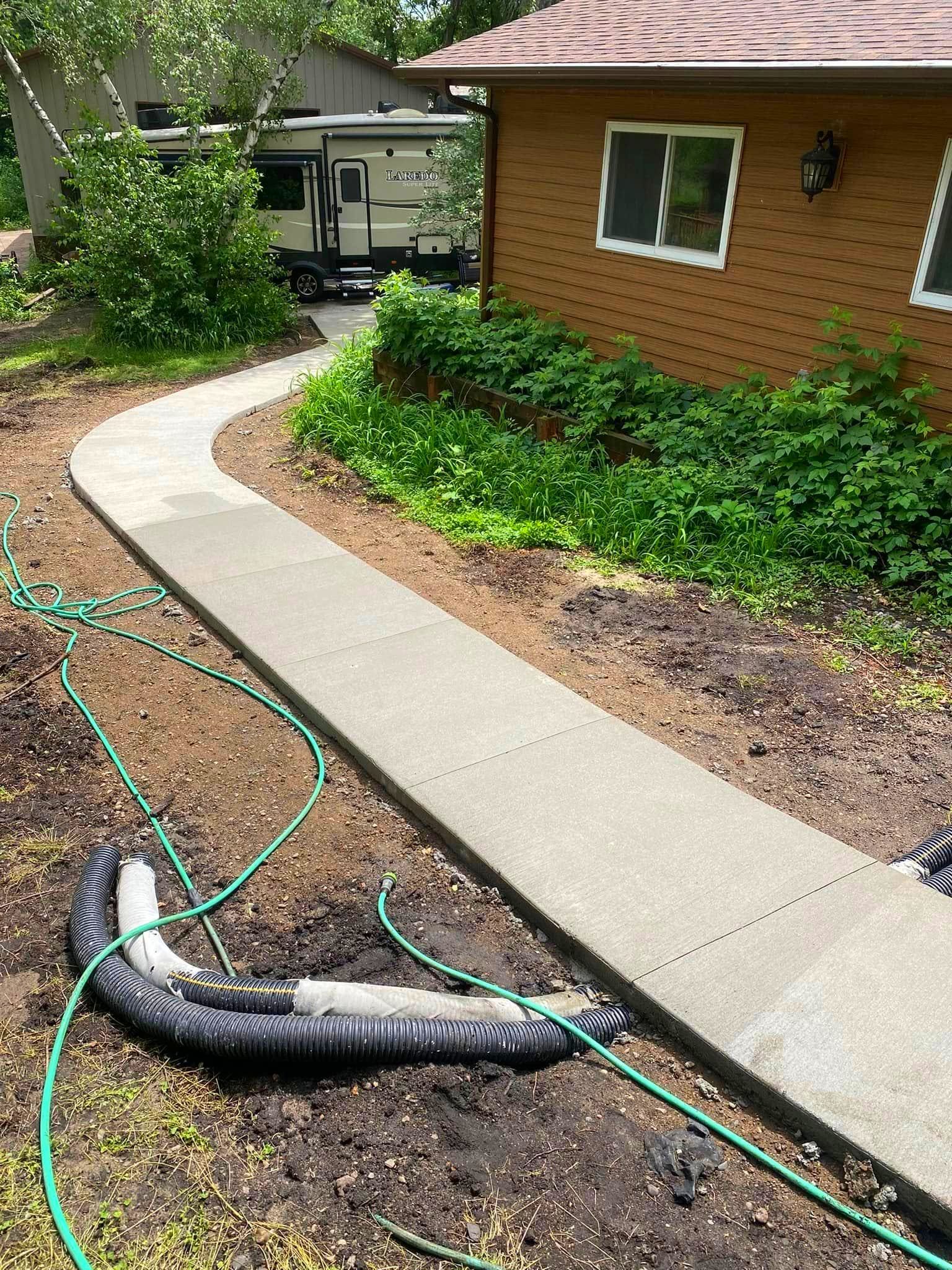 A concrete walkway leading to a house with a hose attached to it.