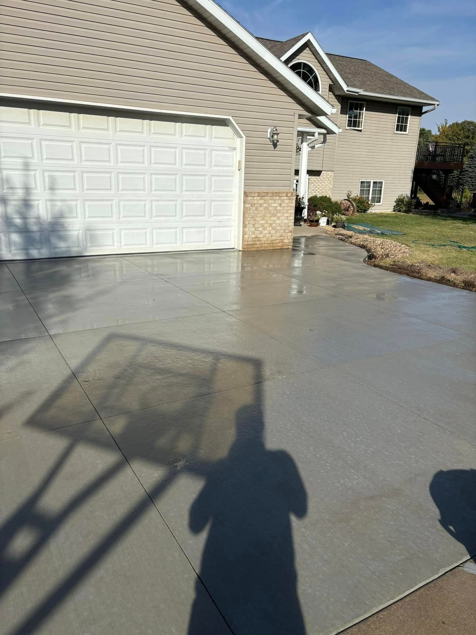 A shadow of a person is cast on a concrete driveway in front of a house.