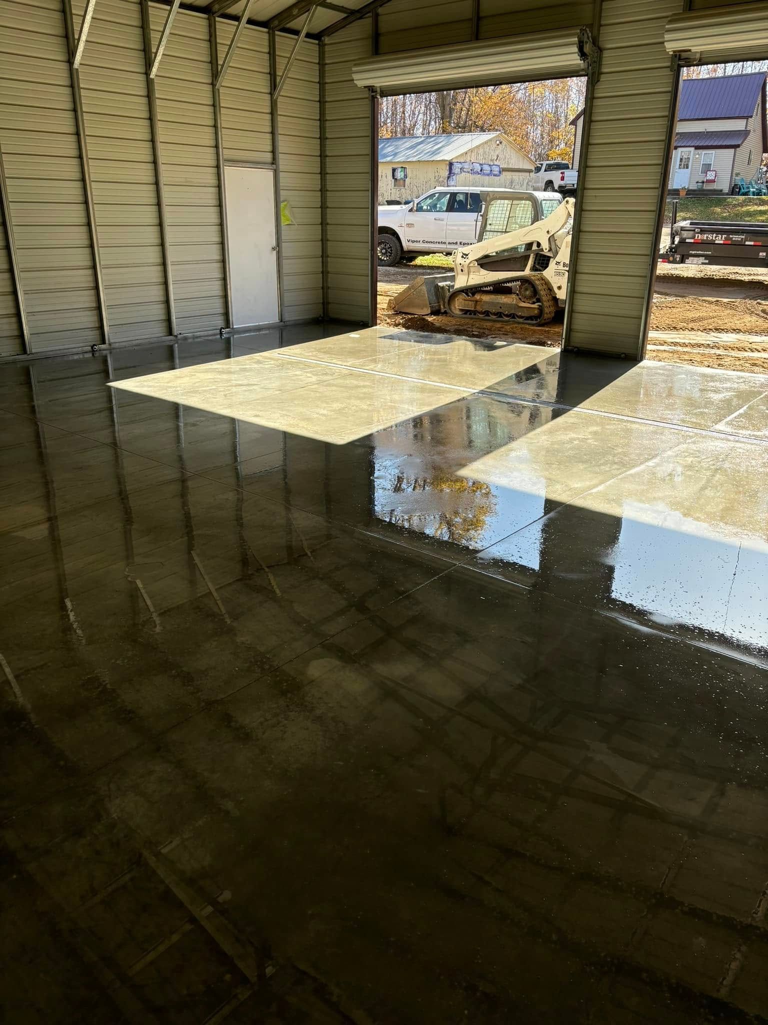 A garage with a lot of water on the floor and a reflection of a bulldozer in the doorway.