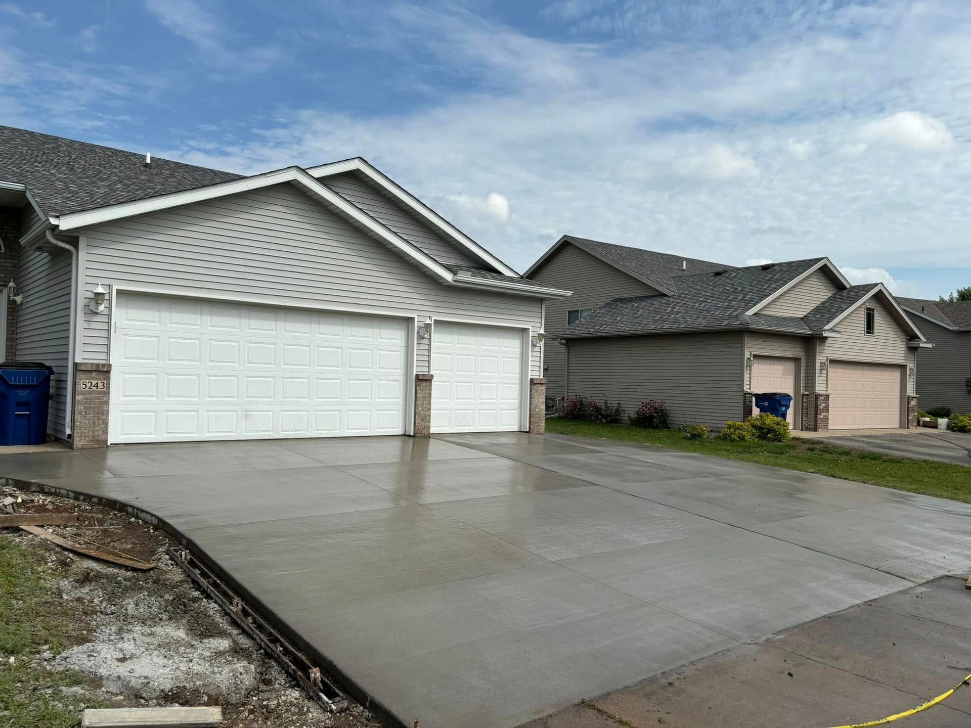 A concrete driveway in front of a house with two garage doors.
