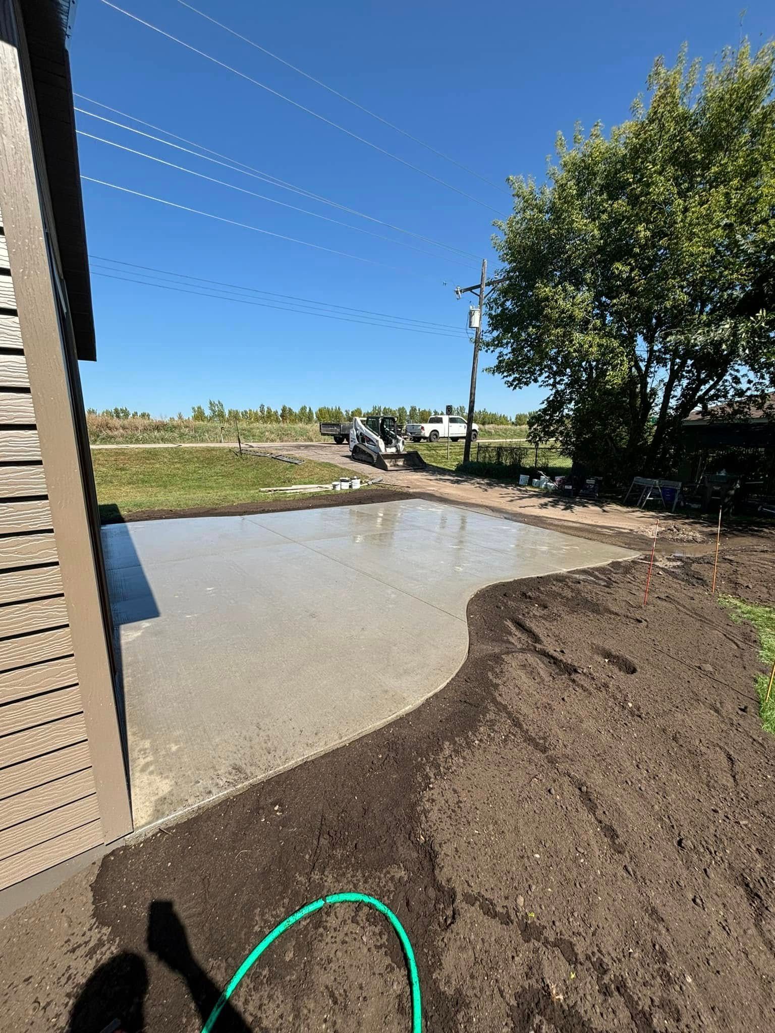 A green hose is laying in the dirt in front of a house.