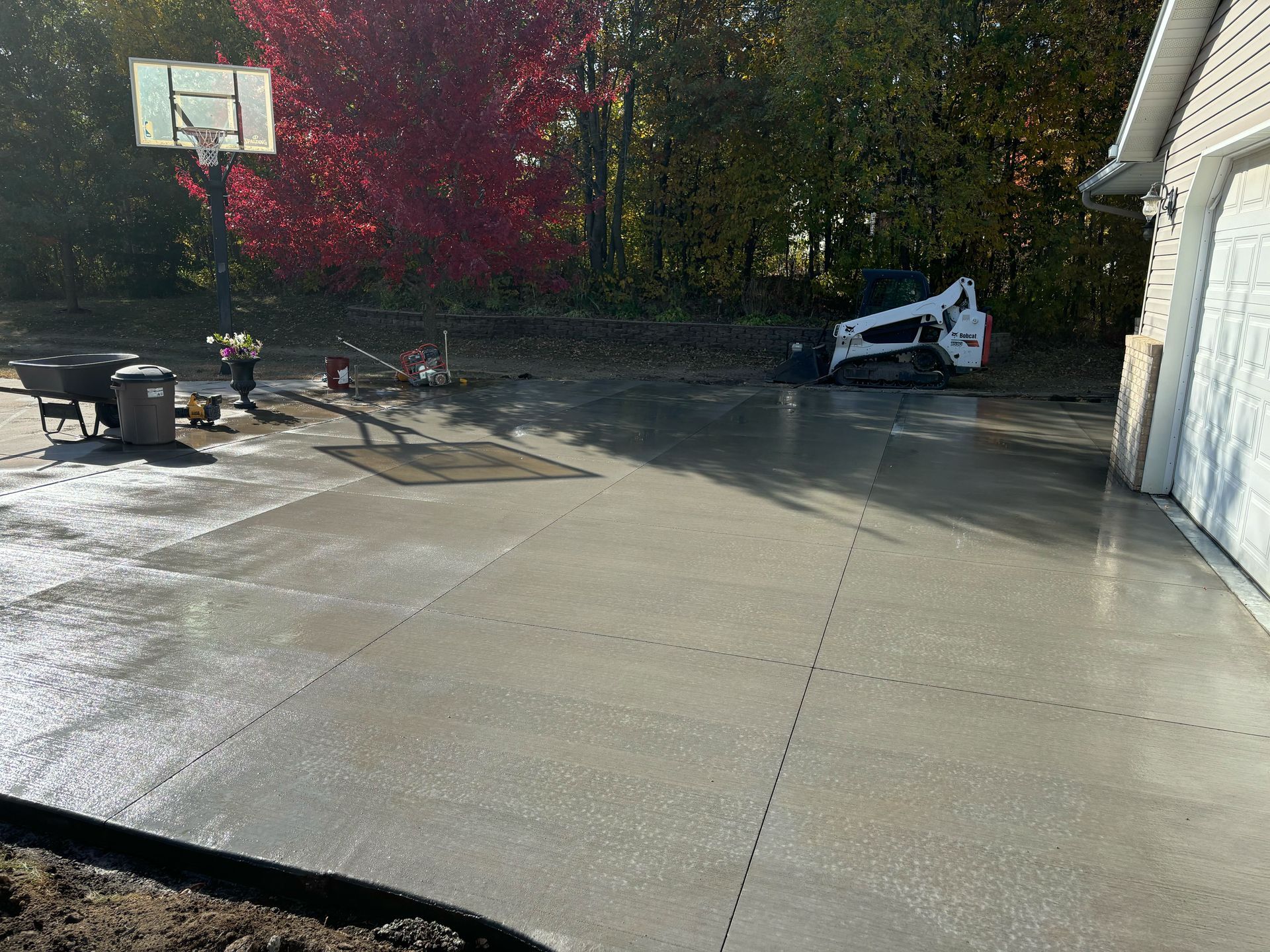 A basketball hoop is being built in a driveway next to a house.