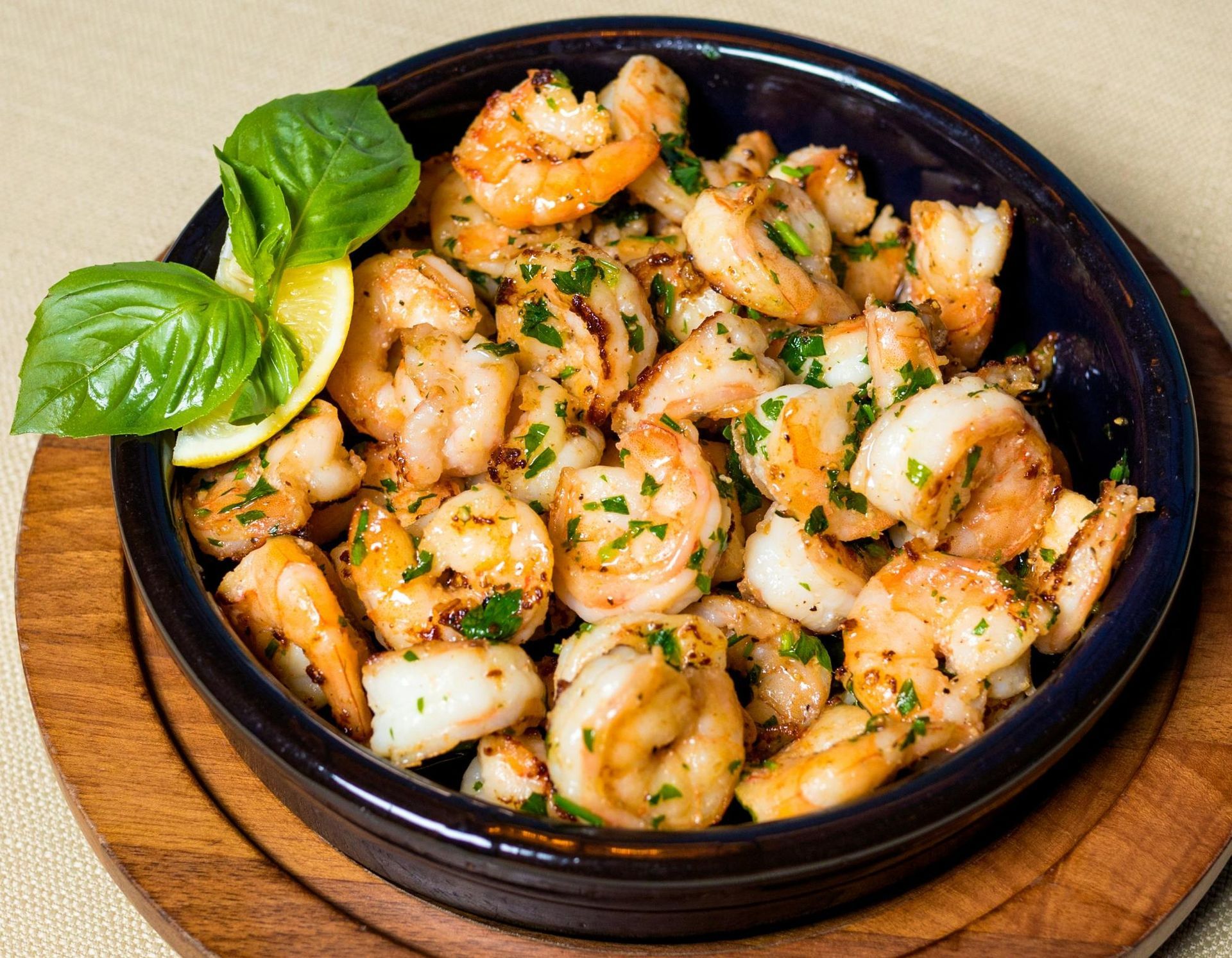 A bowl of garlic shrimp garnished with fresh basil and a lemon wedge, served on a wooden platter.