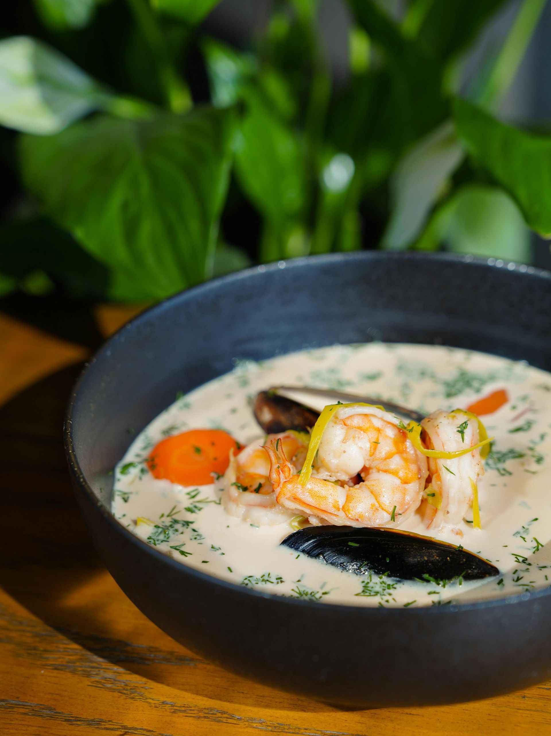 A bowl of creamy seafood soup featuring shrimp, mussels, and sliced carrots, garnished with herbs.