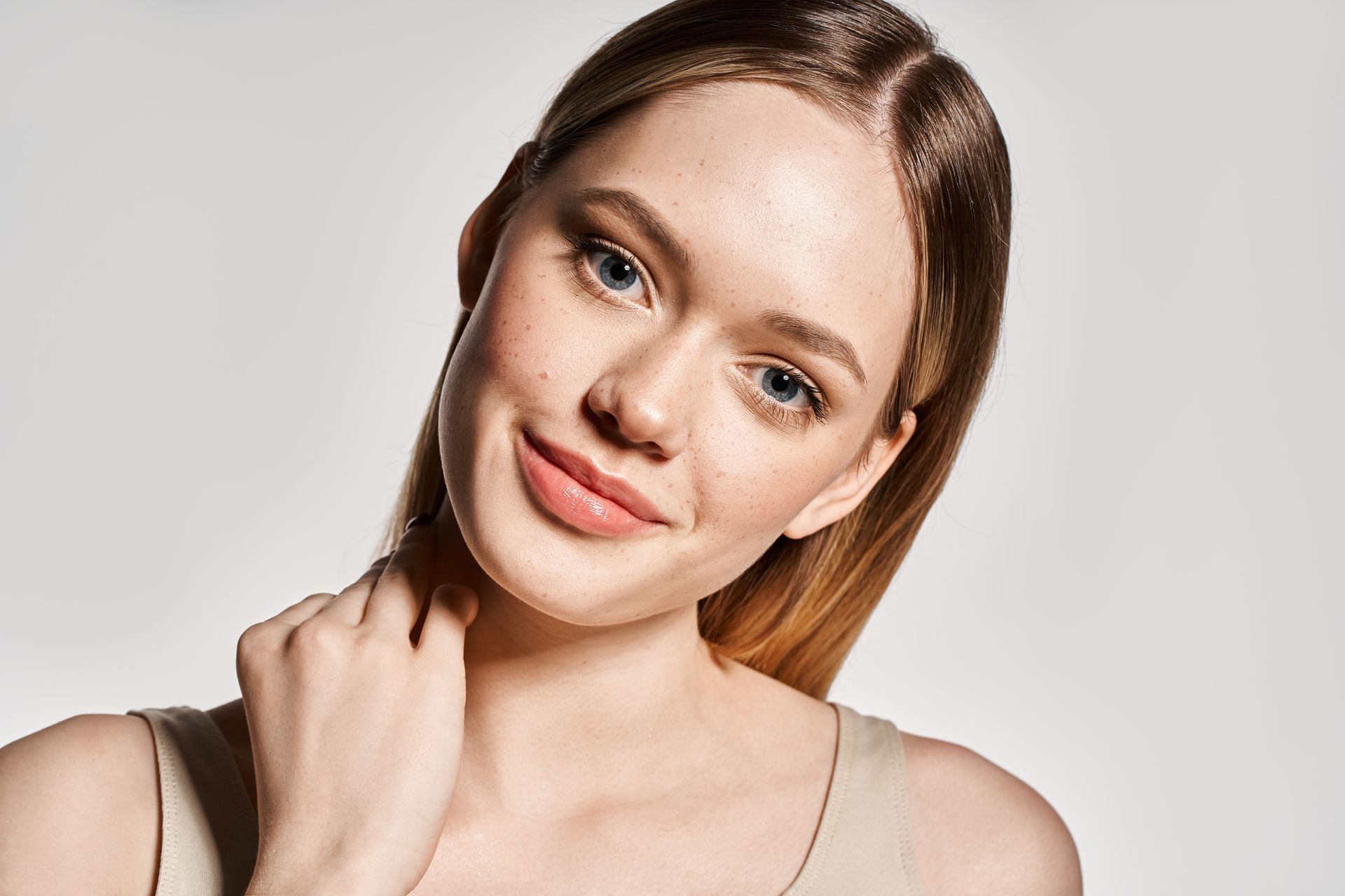 Woman with fair skin, freckles, and light brown hair smiles while touching her neck.