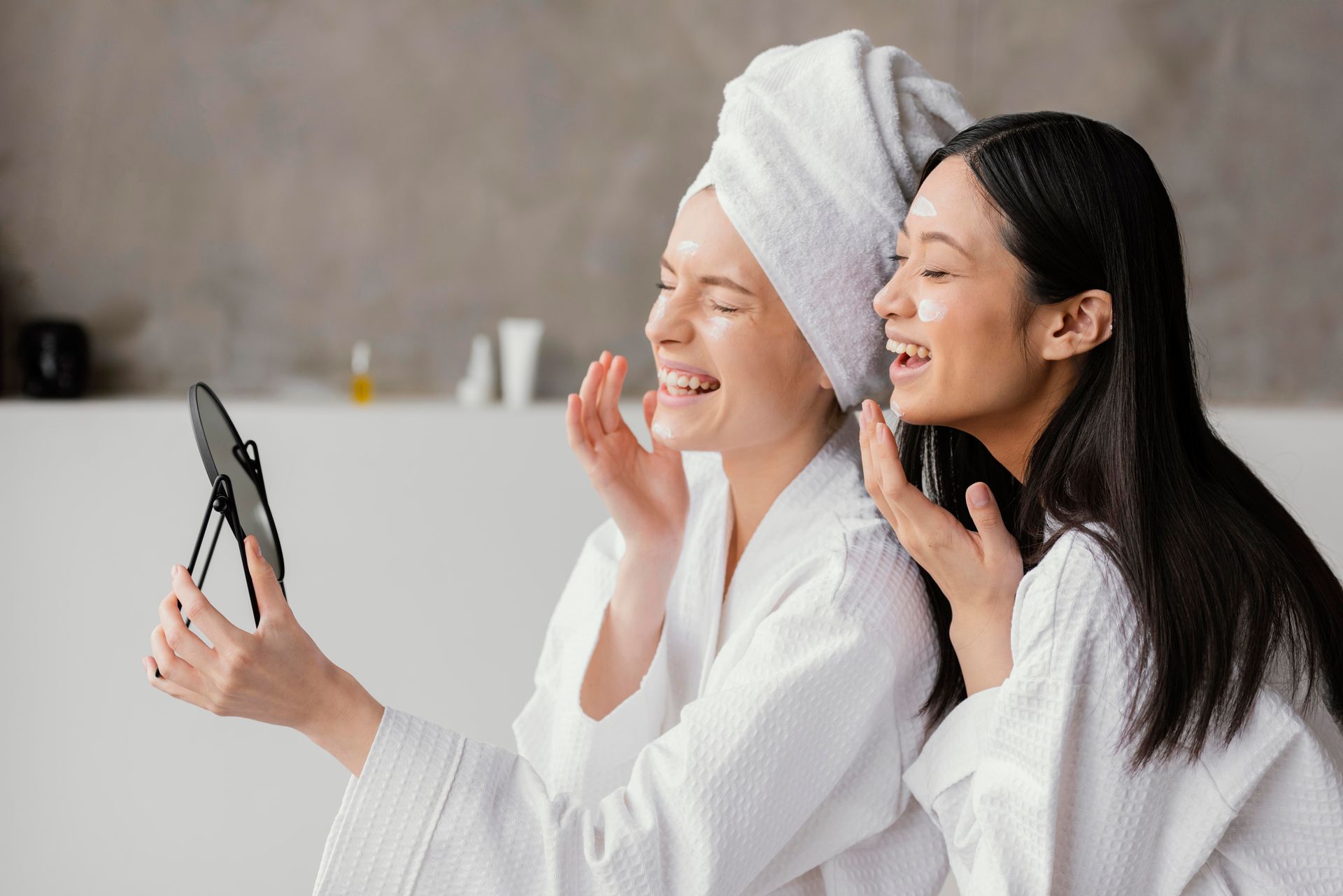 Two women in white robes smiling and taking a selfie in a bright room