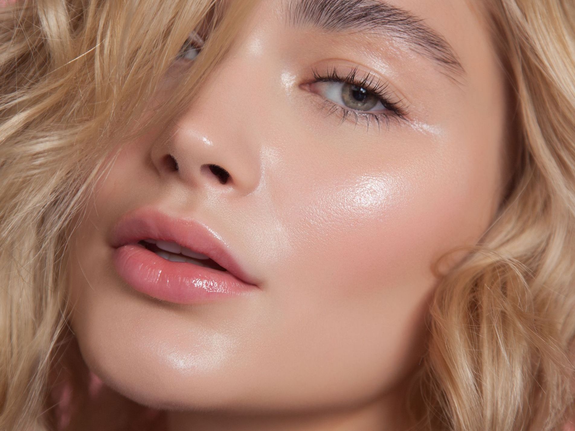Close-up of a fair-skinned woman with blonde hair, glossy lips, and dewy skin with highlights.