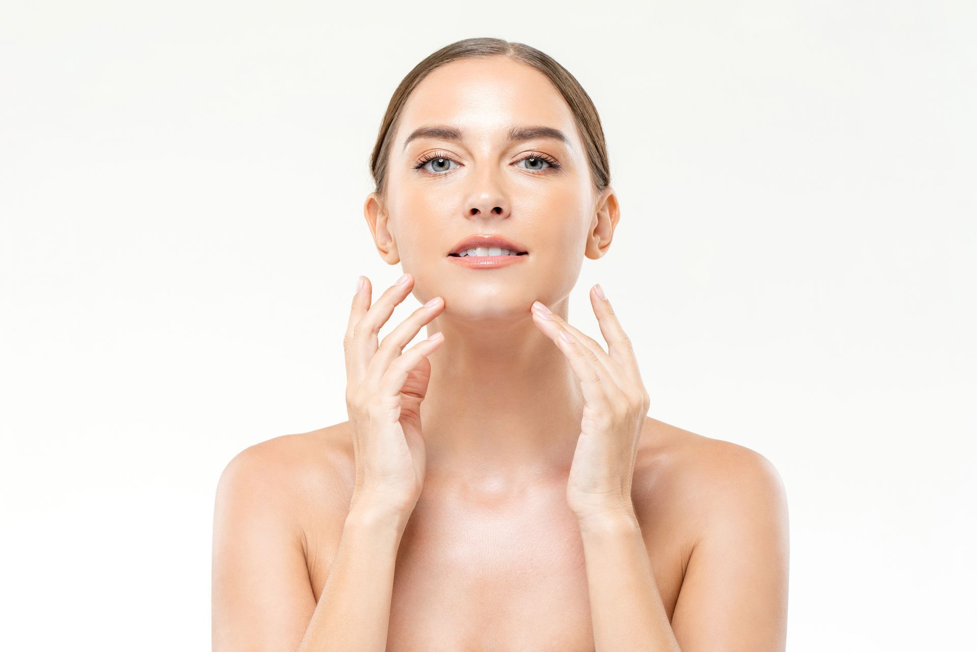 Woman with fair skin and light brown hair, gently touching her face with both hands, looking forward against a light background.