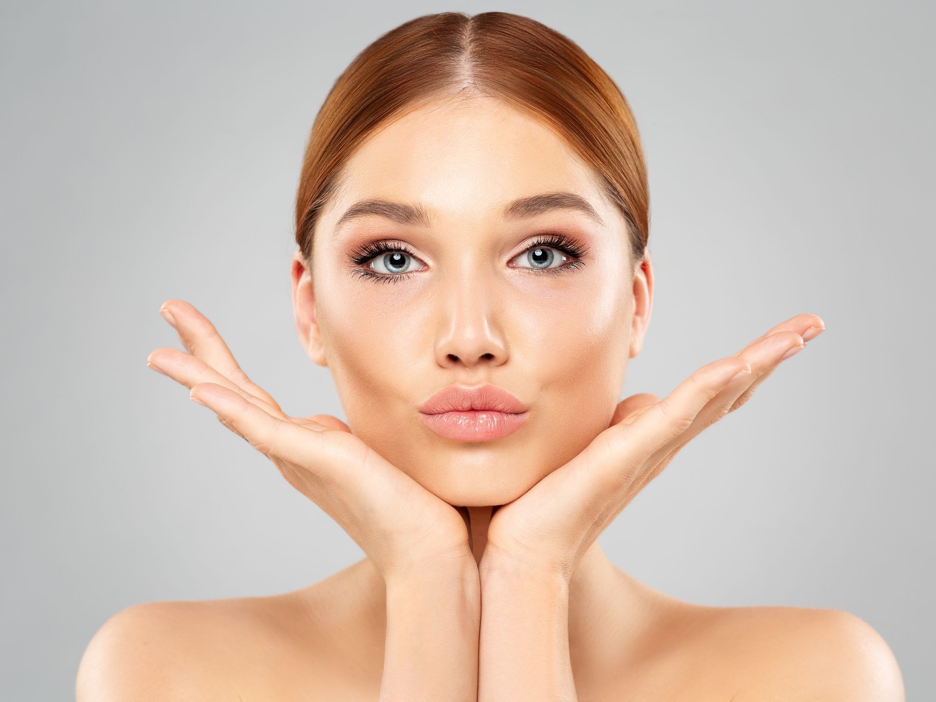 Woman with fair skin, wearing makeup, puckering lips, and holding her hands up near her face.