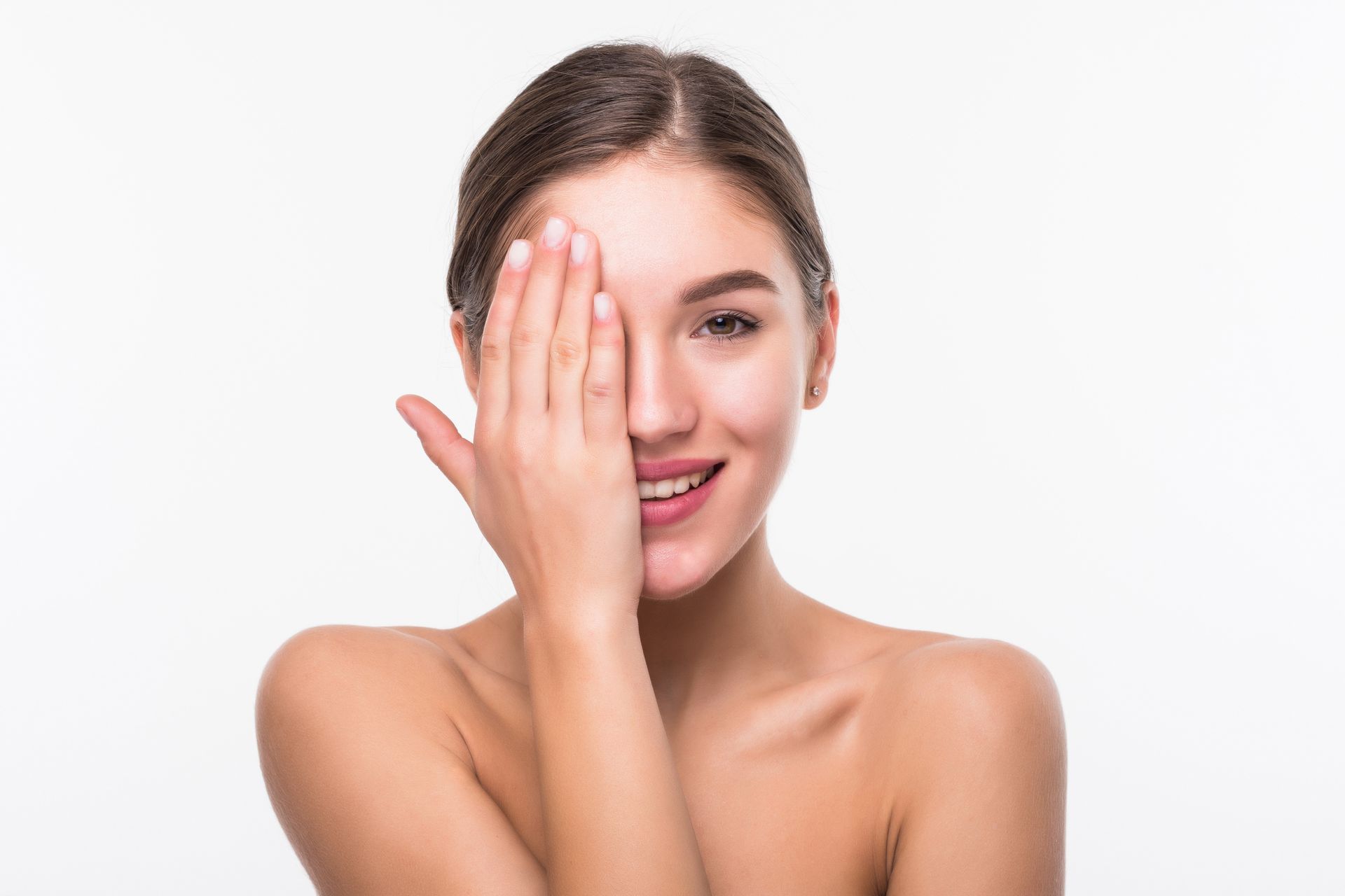 Woman smiling, covering one eye with her hand. She has fair skin, brown hair pulled back, and is set against a white background.