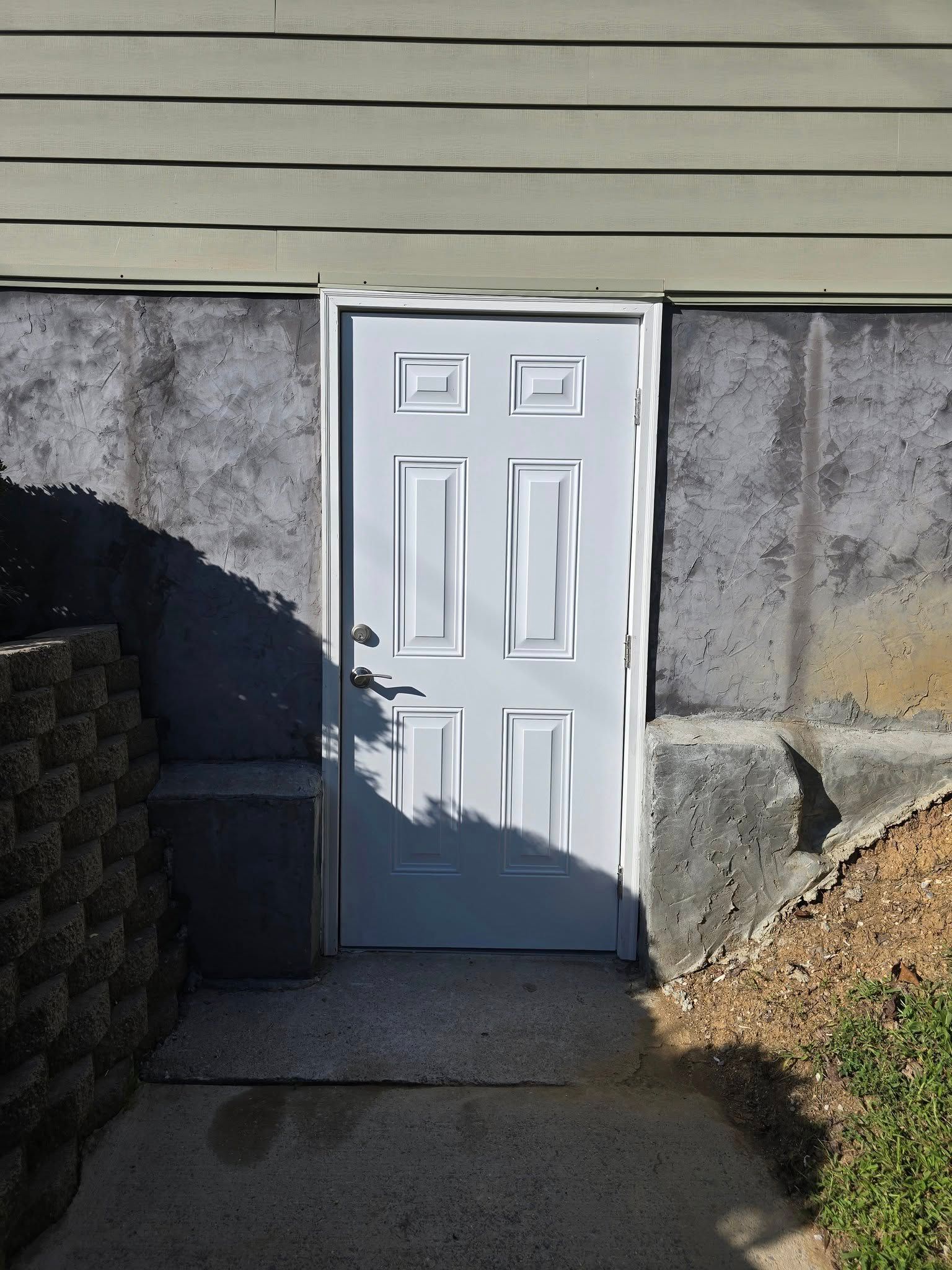 White door set into concrete foundation. Sunlight casts shadow.