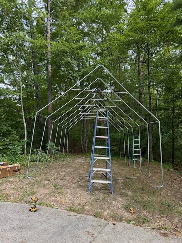 Metal frame of a building in progress, with a ladder in the middle. Trees surround the structure.