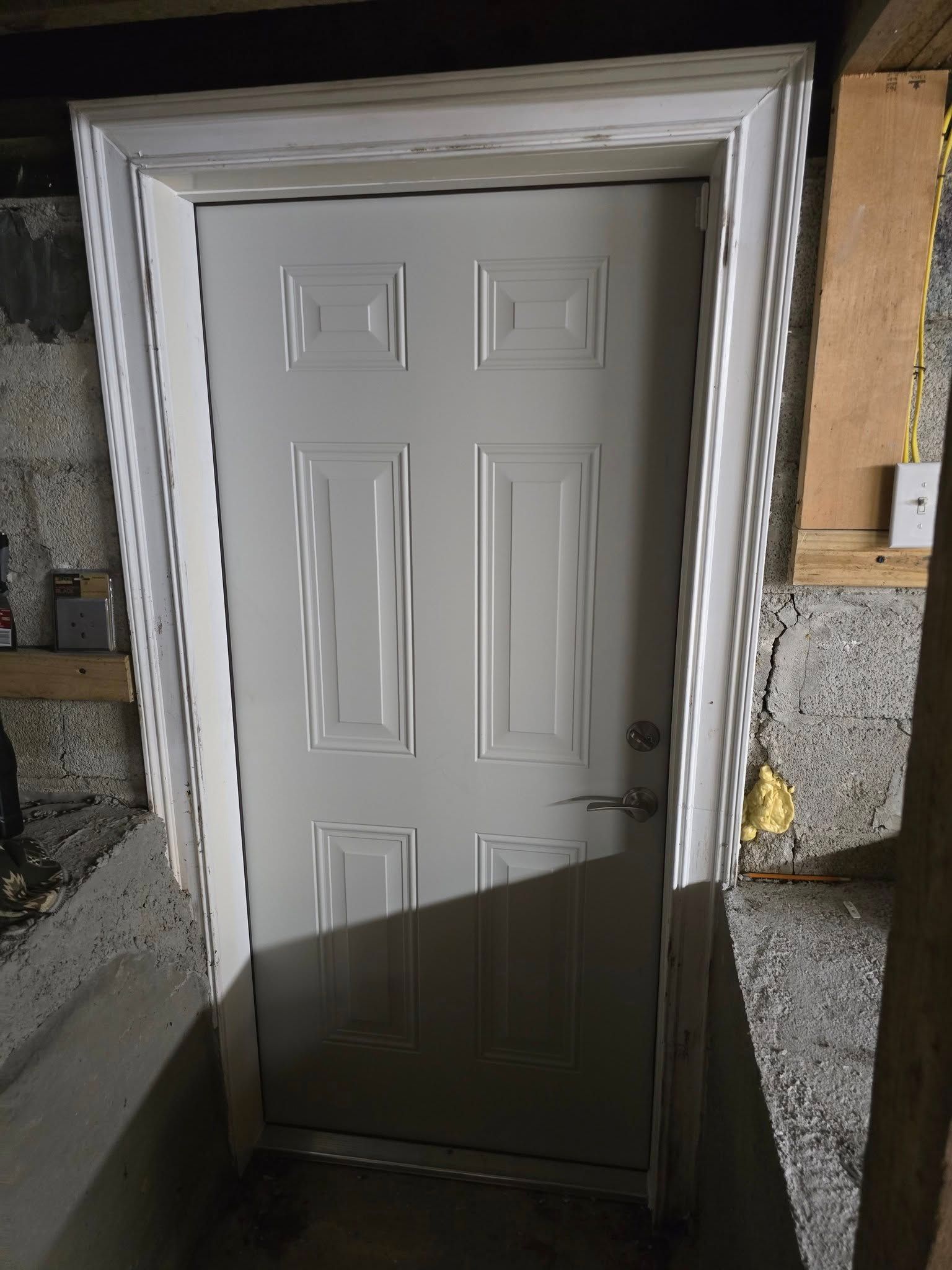 White door with six panels in a concrete and wood framed doorway.