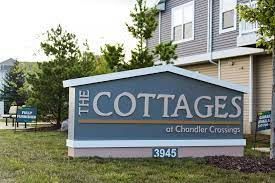 Sign for The Cottages at Chandler Crossings, grey with white letters, green grass and building in the background.