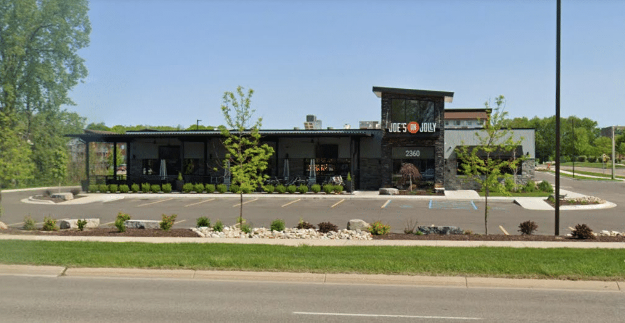 Restaurant exterior with stone facade, dark roof, and parking lot. Landscaped with rocks and small trees.