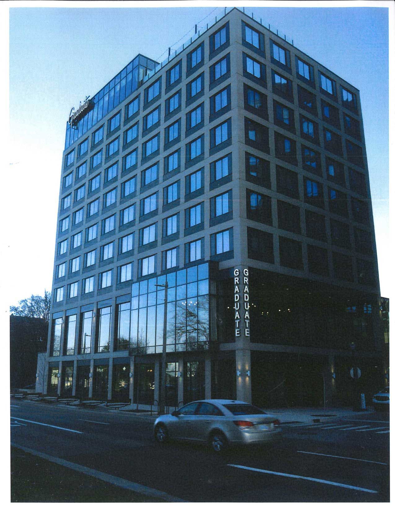 Modern, multi-story building with glass facade; car drives by on street in front.