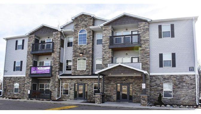 Apartment building with stone and grey siding, balconies, and dark shutters.