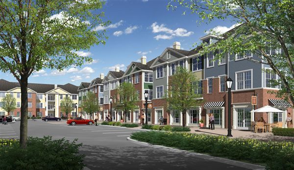 Row of townhouses with shops, trees, and a red car on a sunny day.