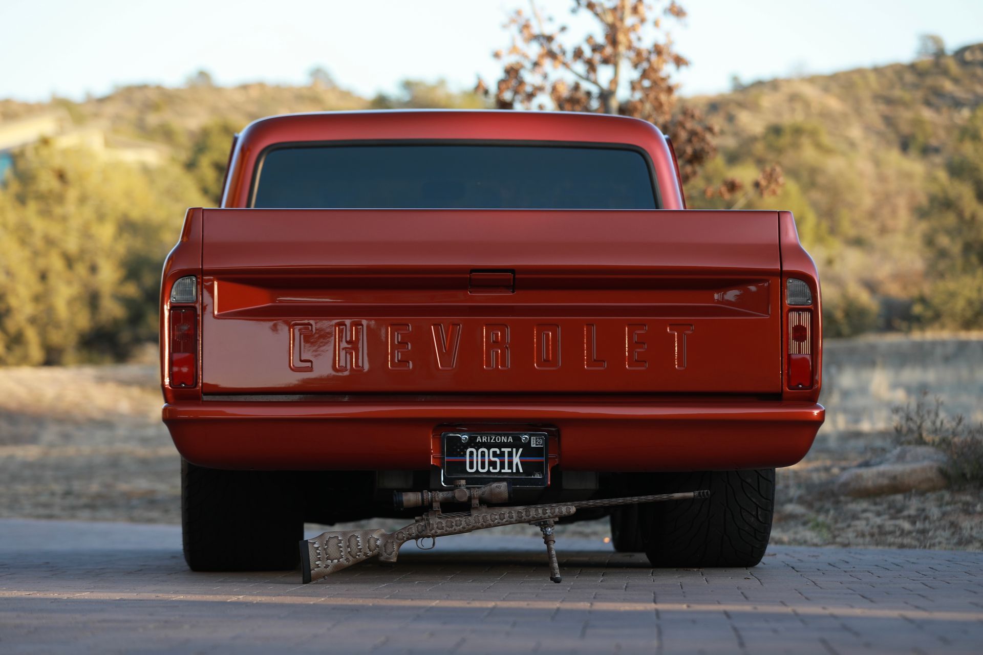 Rear view of a red Chevrolet truck with a rifle resting beneath the bumper, license plate reads 