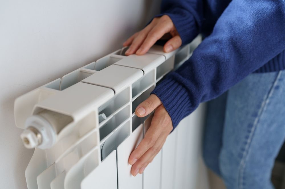 A person is adjusting a radiator on a wall.