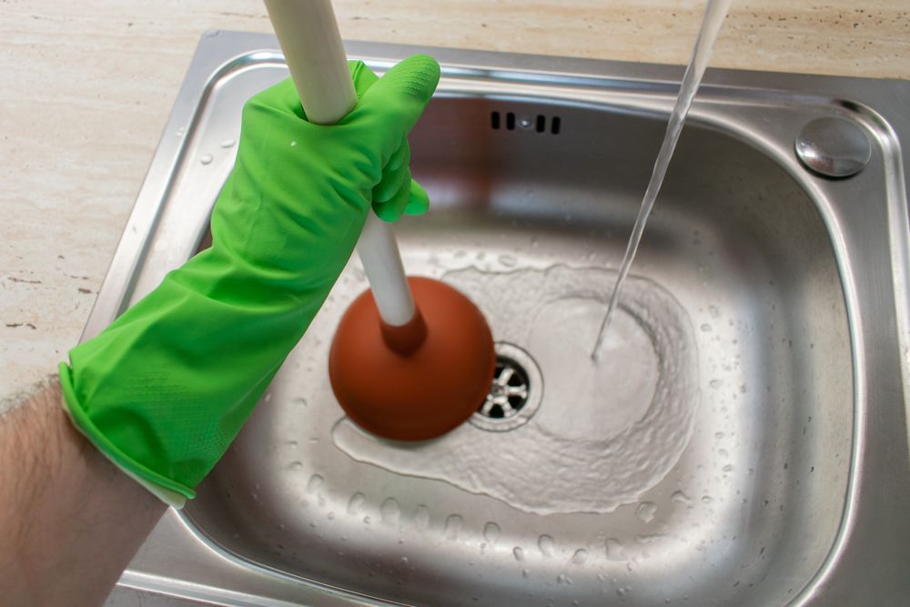 A person is using a plunger to unblock a sink.