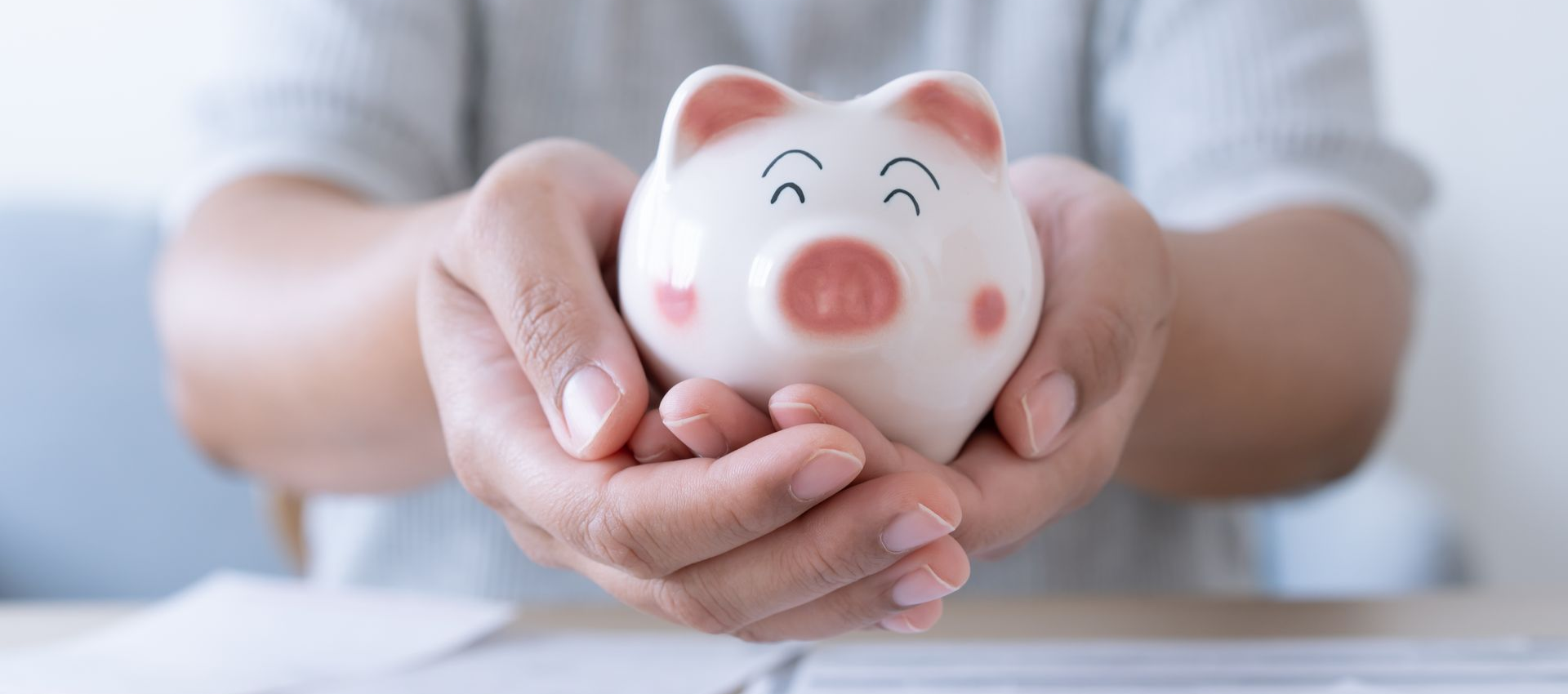 Hands holding a white piggy bank with a pink nose and ears.